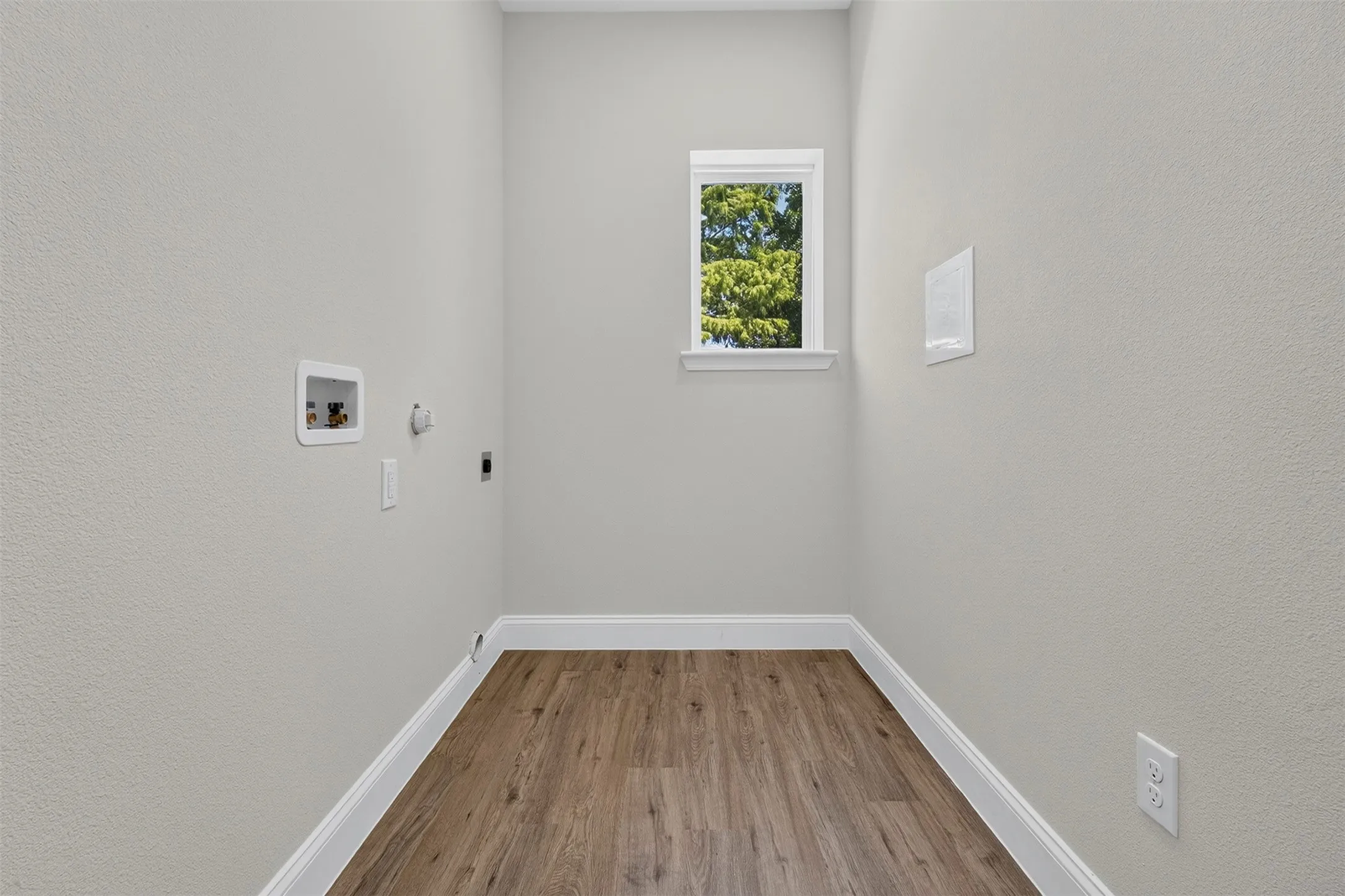 Wood-finish flooring, white trim, and a window with natural light