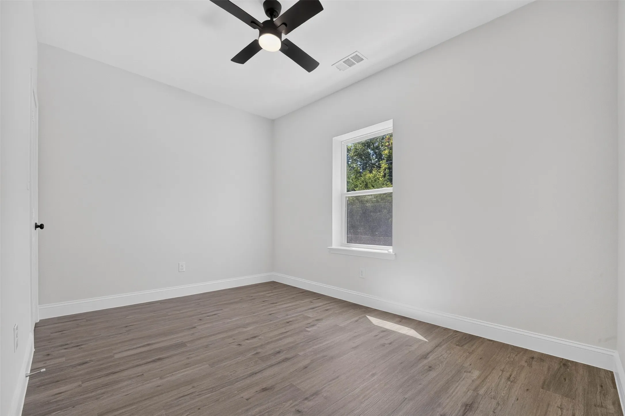 Wood-finish flooring with white trim, a single window, and a ceiling fan with integrated lighting