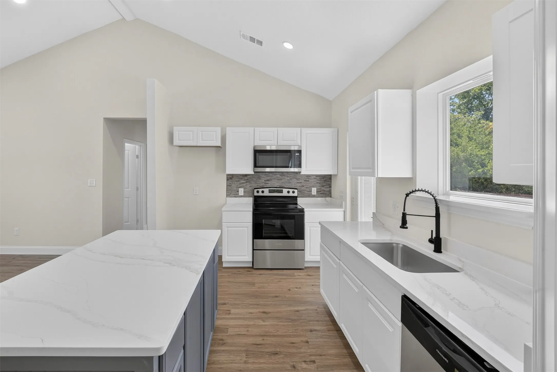 Vaulted ceiling kitchen featuring white cabinetry, light-toned countertops, stainless steel appliances, and wood-finish flooring