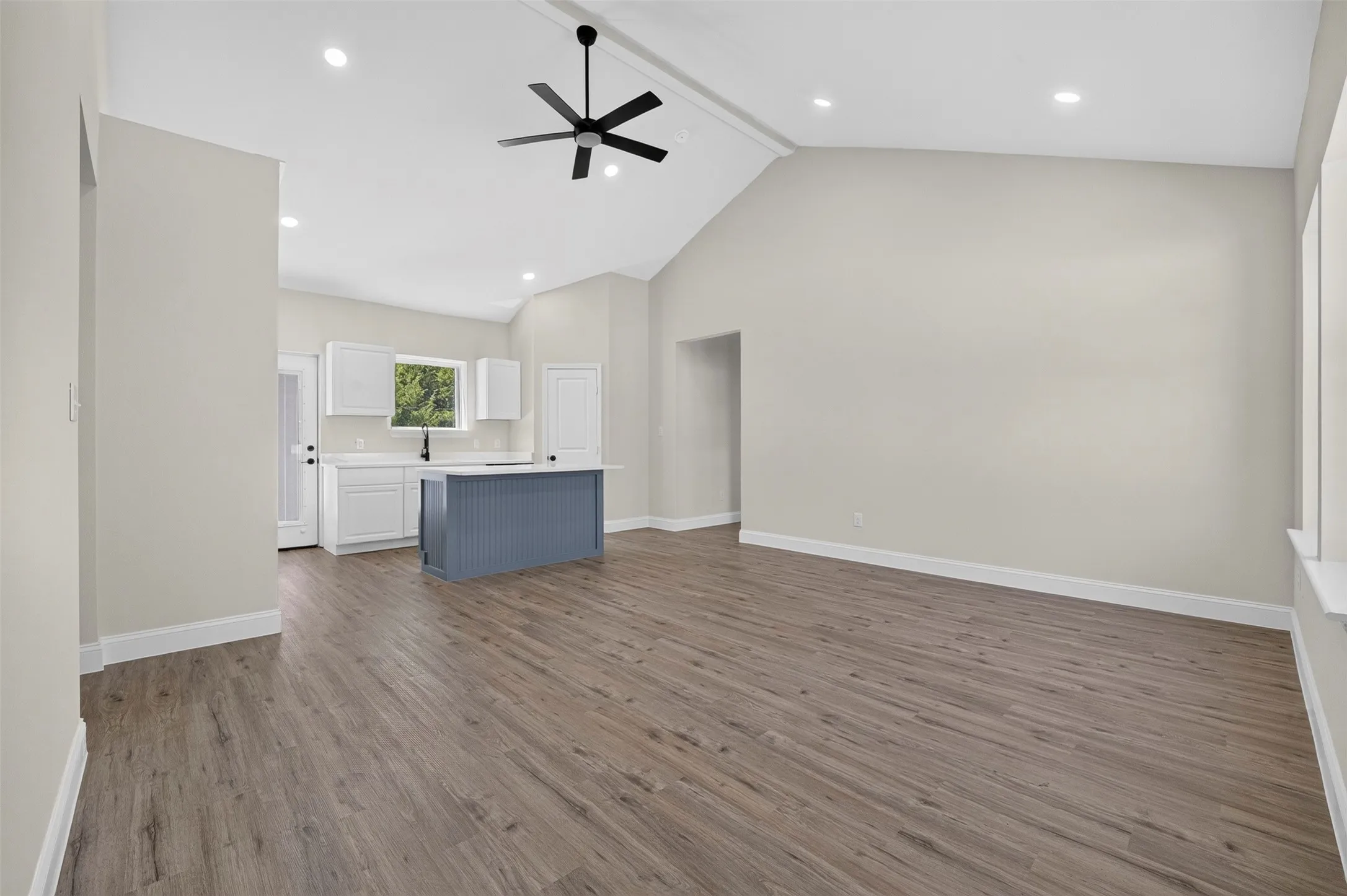 Vaulted ceiling, recessed lighting, wood-finish flooring, white cabinetry, and a blue island