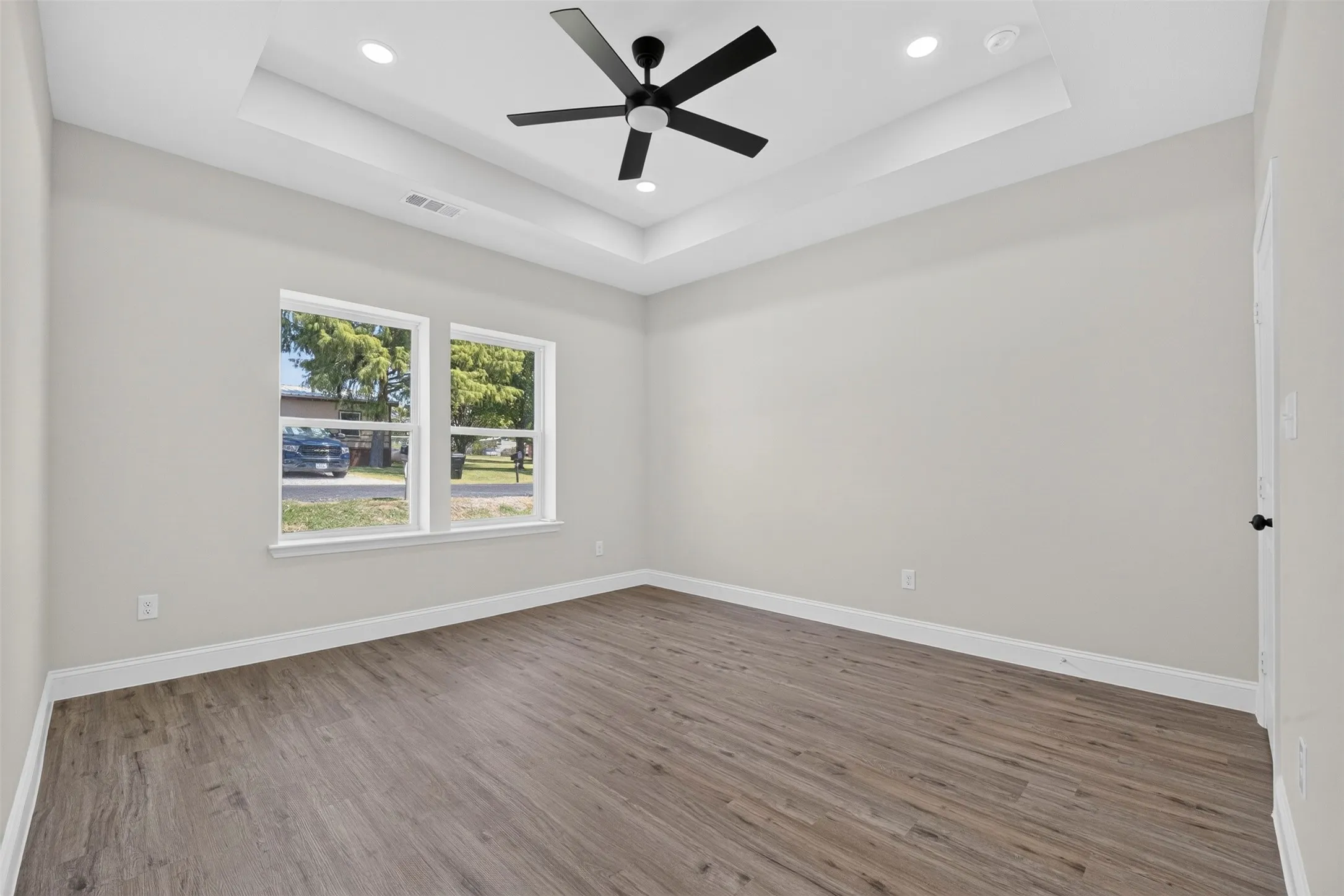Tray ceiling with recessed lighting and a ceiling fan, dual windows, wood-finish flooring, and light neutral wall paint