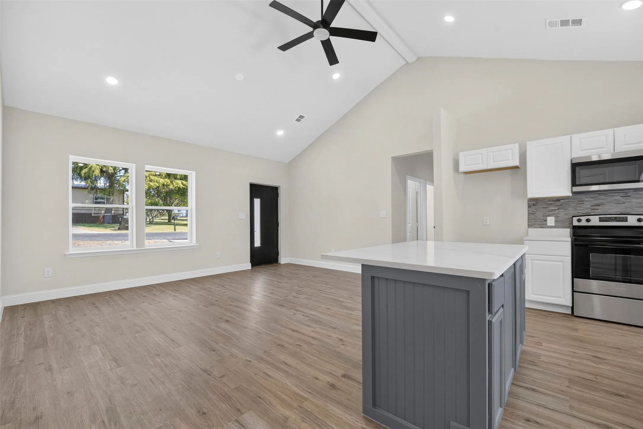 Vaulted ceilings, wood-finish flooring, recessed lighting, kitchen island with solid surface countertop, and stainless steel appliances