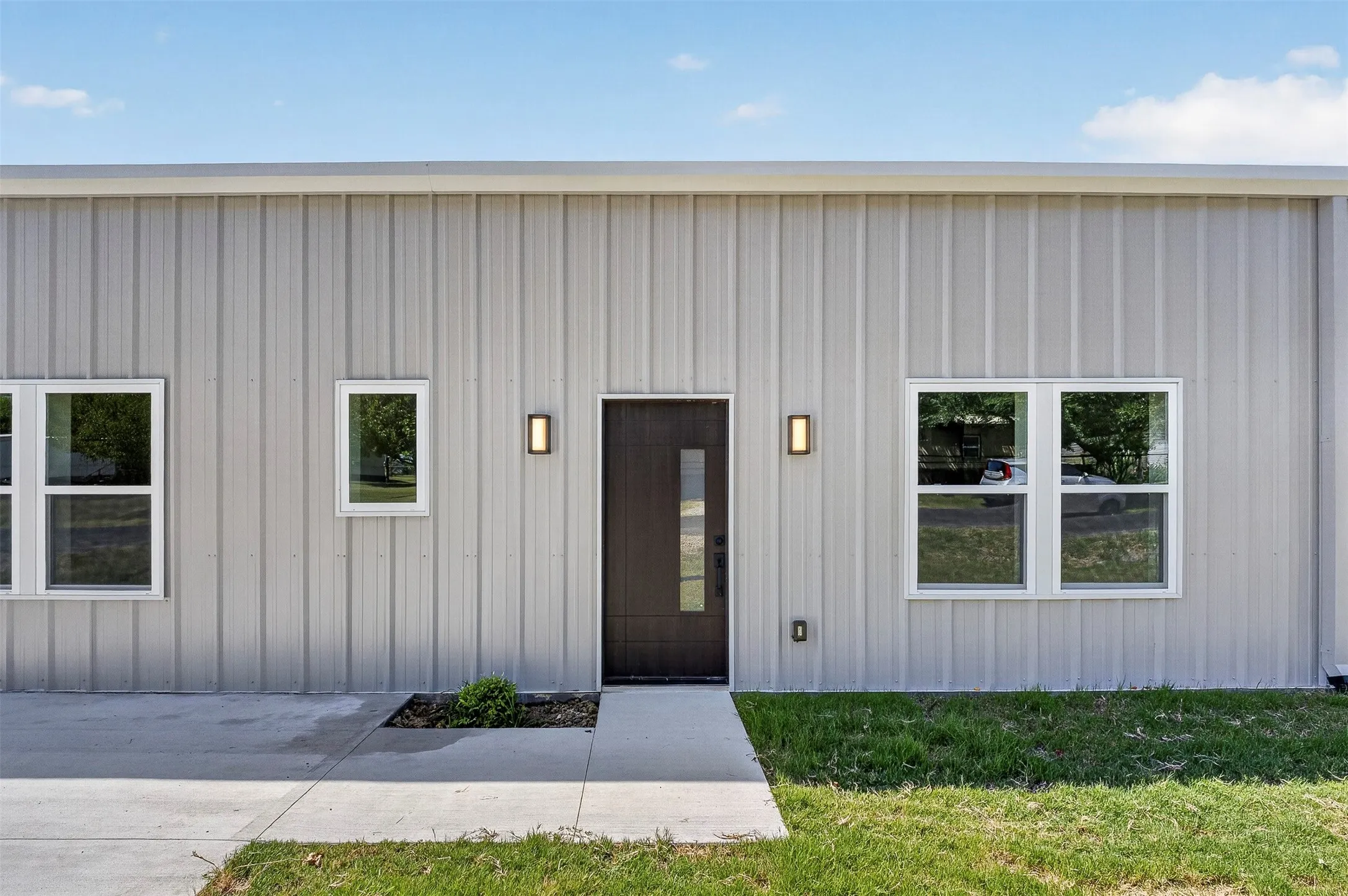 Modern industrial front elevation featuring corrugated metal exterior cladding, black entry door with sidelite window, and multiple casement windows with dark frames