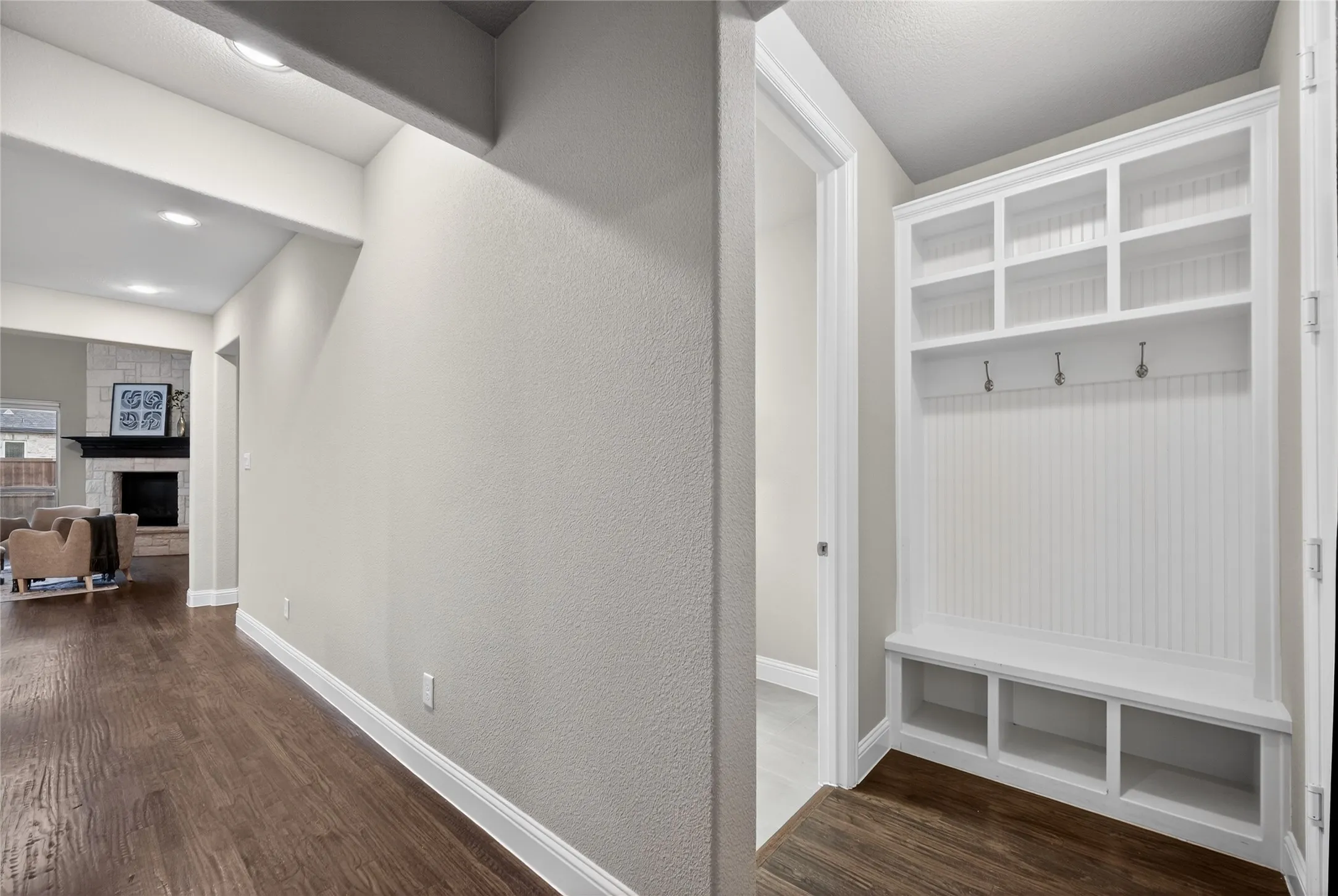 Built-in mudroom bench with storage cubbies and upper shelving, wood-finish flooring, recessed lighting, and a stone-surround fireplace visible in the background