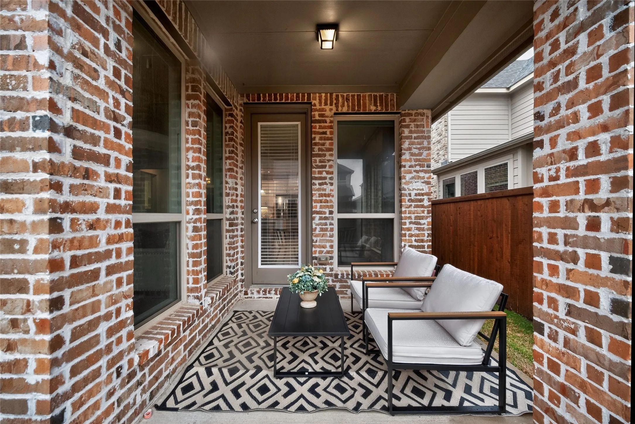 Covered patio featuring brick exterior walls, a built-in outdoor light fixture, and a glass-paneled door