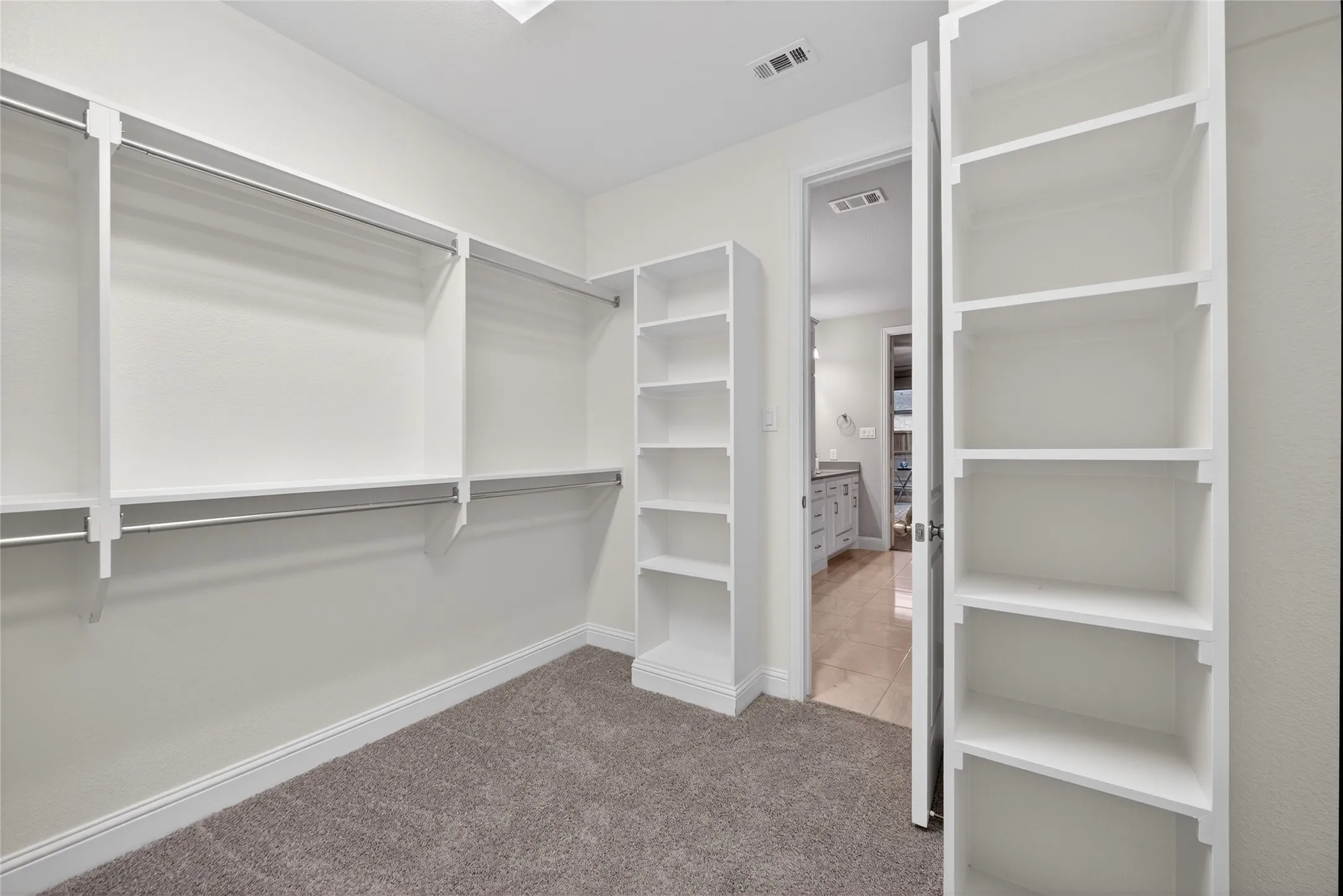 Walk-in closet featuring white built-in shelving, hanging rods, and grey carpeting