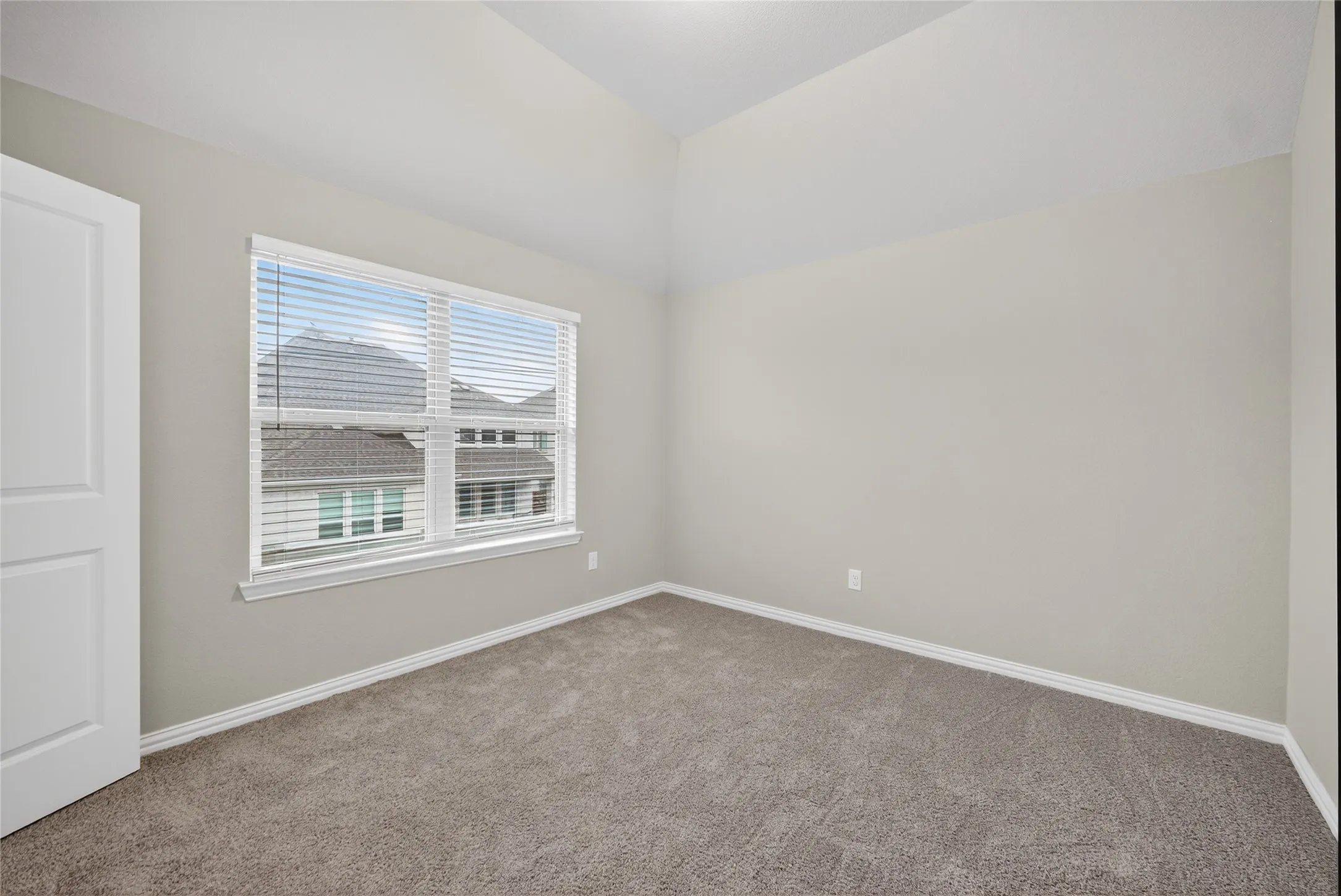 Vaulted ceiling, neutral wall paint, carpet flooring, and a window with horizontal blinds