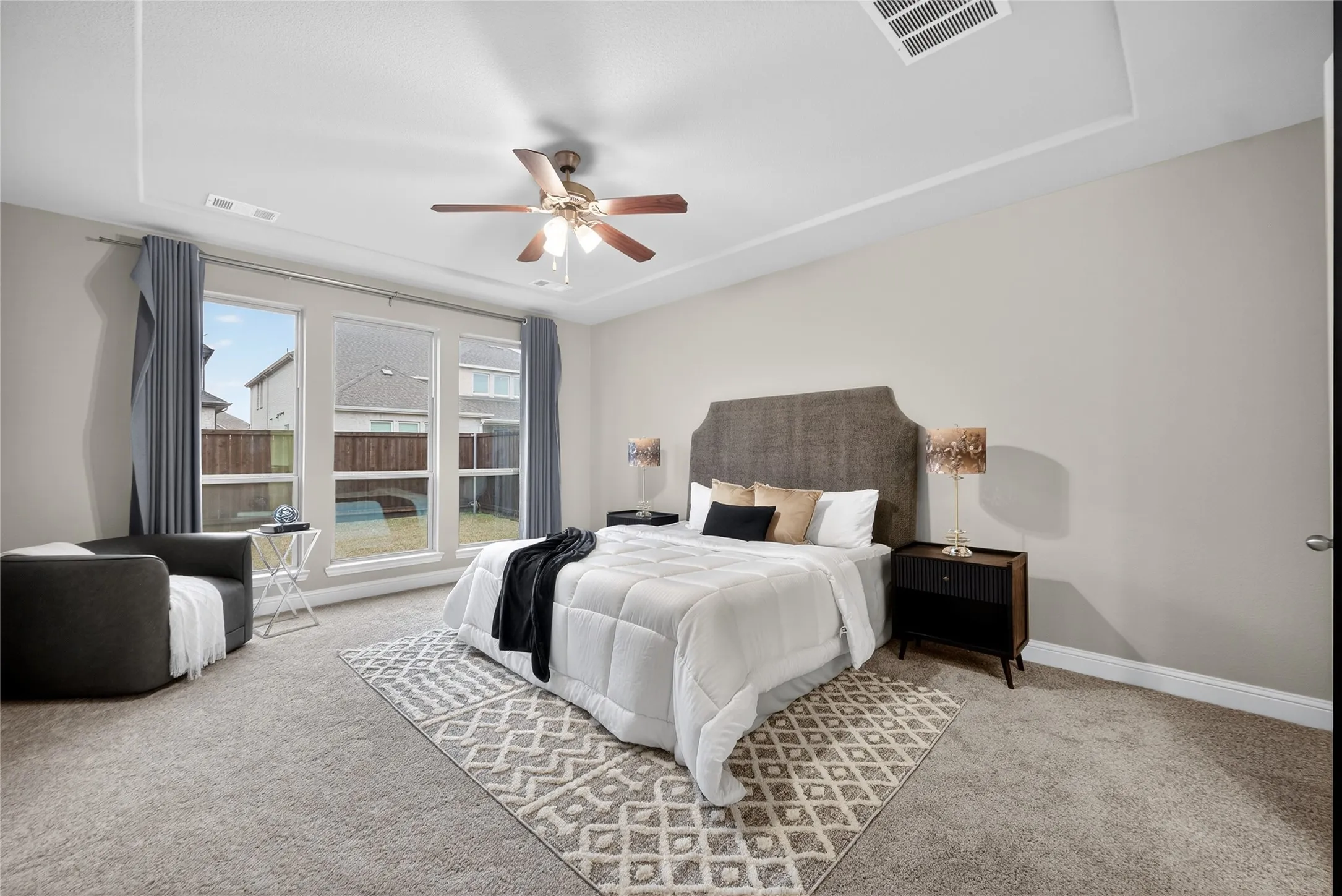 Tray ceiling with a ceiling fan, three pane windows, and neutral wall paint
