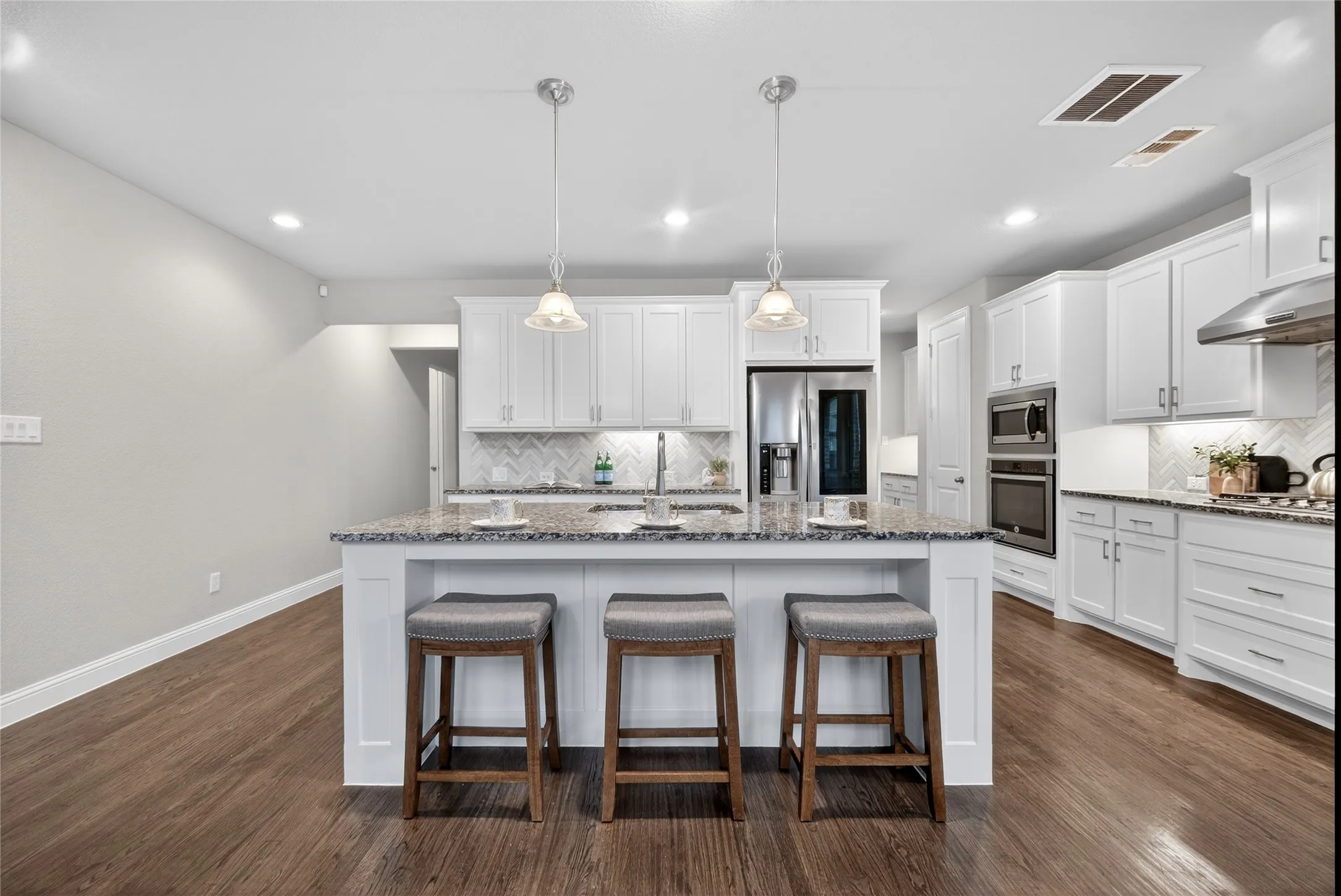 Kitchen featuring a large island with pendant lighting, white cabinetry, integrated stainless steel appliances, a tile backsplash, and wood-finish flooring