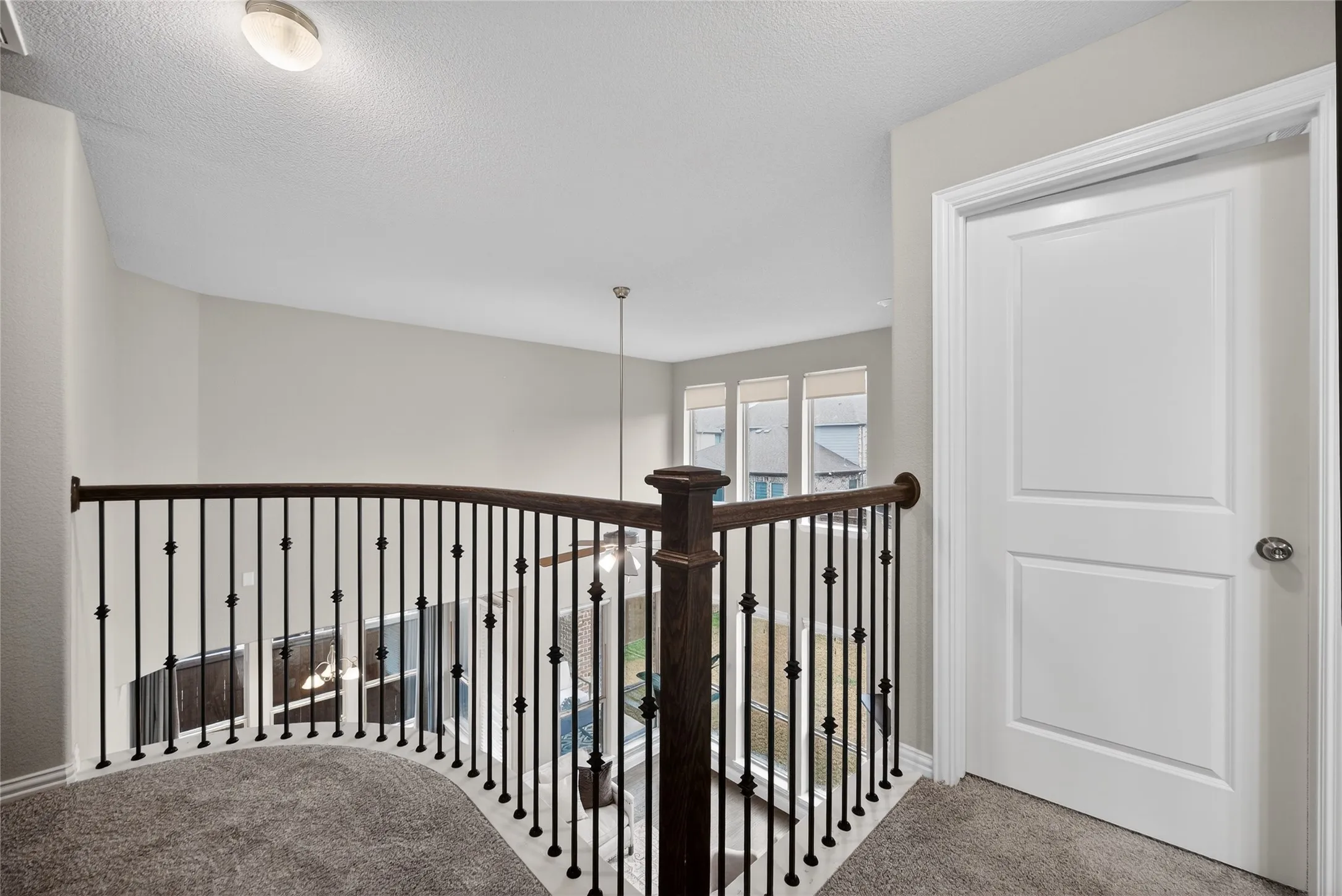 Curved wood and iron spindle railing overlooking an open space, with recessed lighting, carpeting, and a panel door