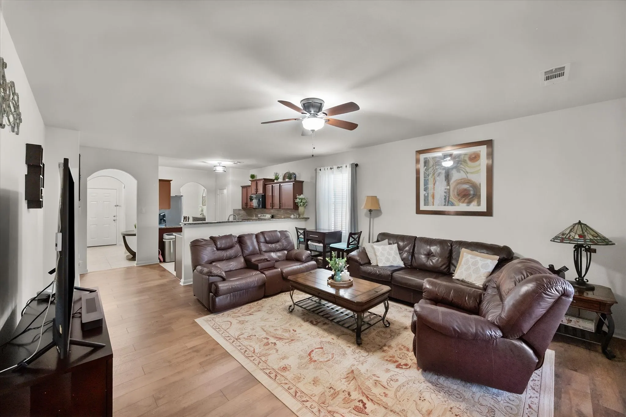 Open-concept living area featuring wood-finish flooring, a ceiling fan, and recessed archways leading to additional spaces