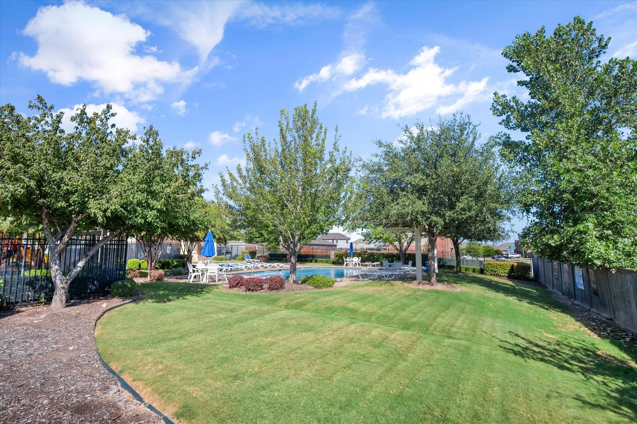 Expansive lawn area with mature trees, surrounded by a black metal fence and wood fence
