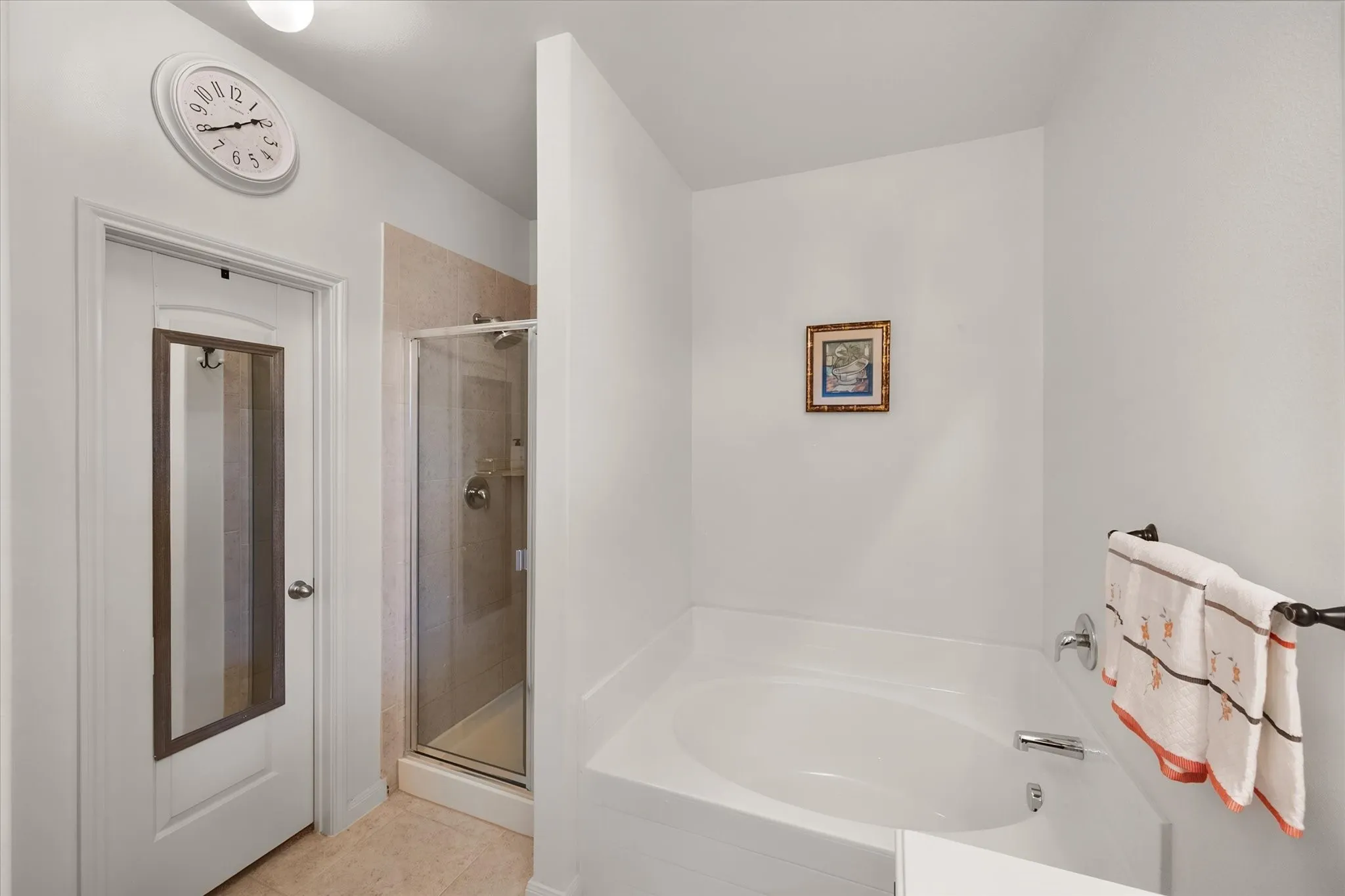Built-in soaking tub, glass-enclosed shower, tiled shower surround, chrome plumbing fixtures, and a white interior door with a mirrored panel