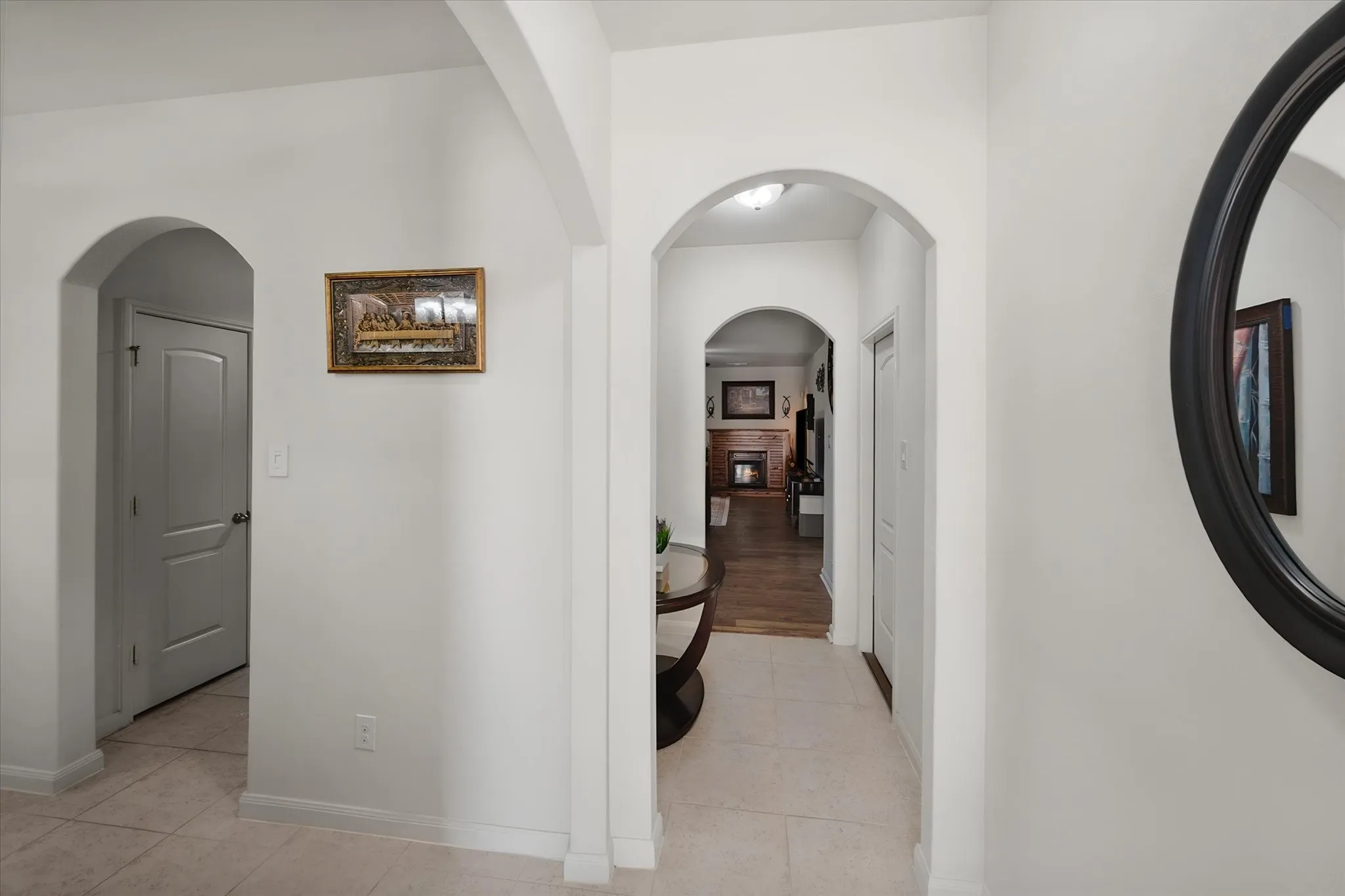 Elegant hallway with arched doorways, neutral white walls, and tile flooring throughout
