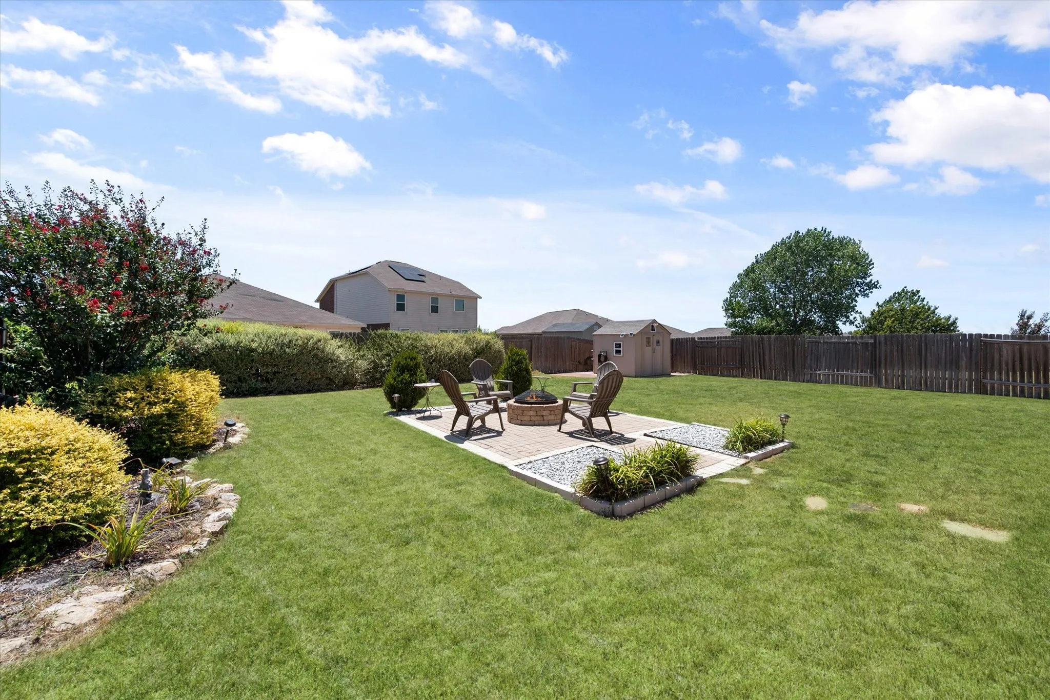 Expansive backyard featuring a paver patio with a built-in fire pit, a wooden storage shed, and a privacy fence