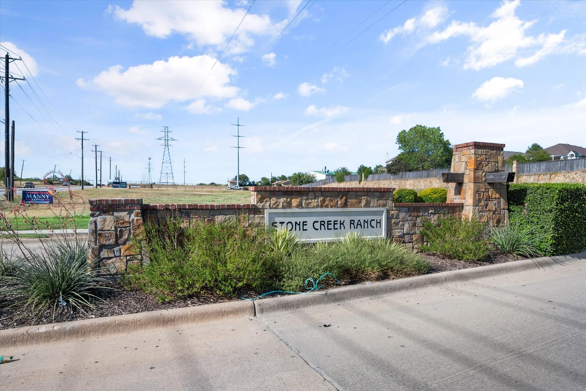 Stone Creek Ranch signage set within a natural stone and brick wall, featuring manicured shrubs and ground cover