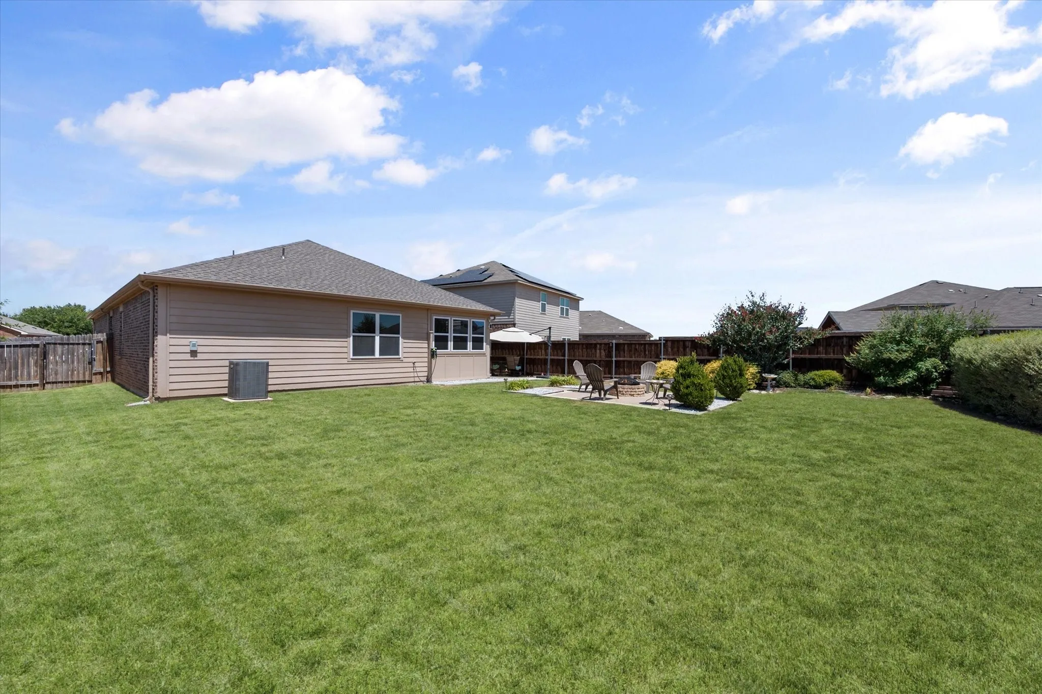 Expansive backyard featuring a manicured lawn, a stone patio, and perimeter fencing