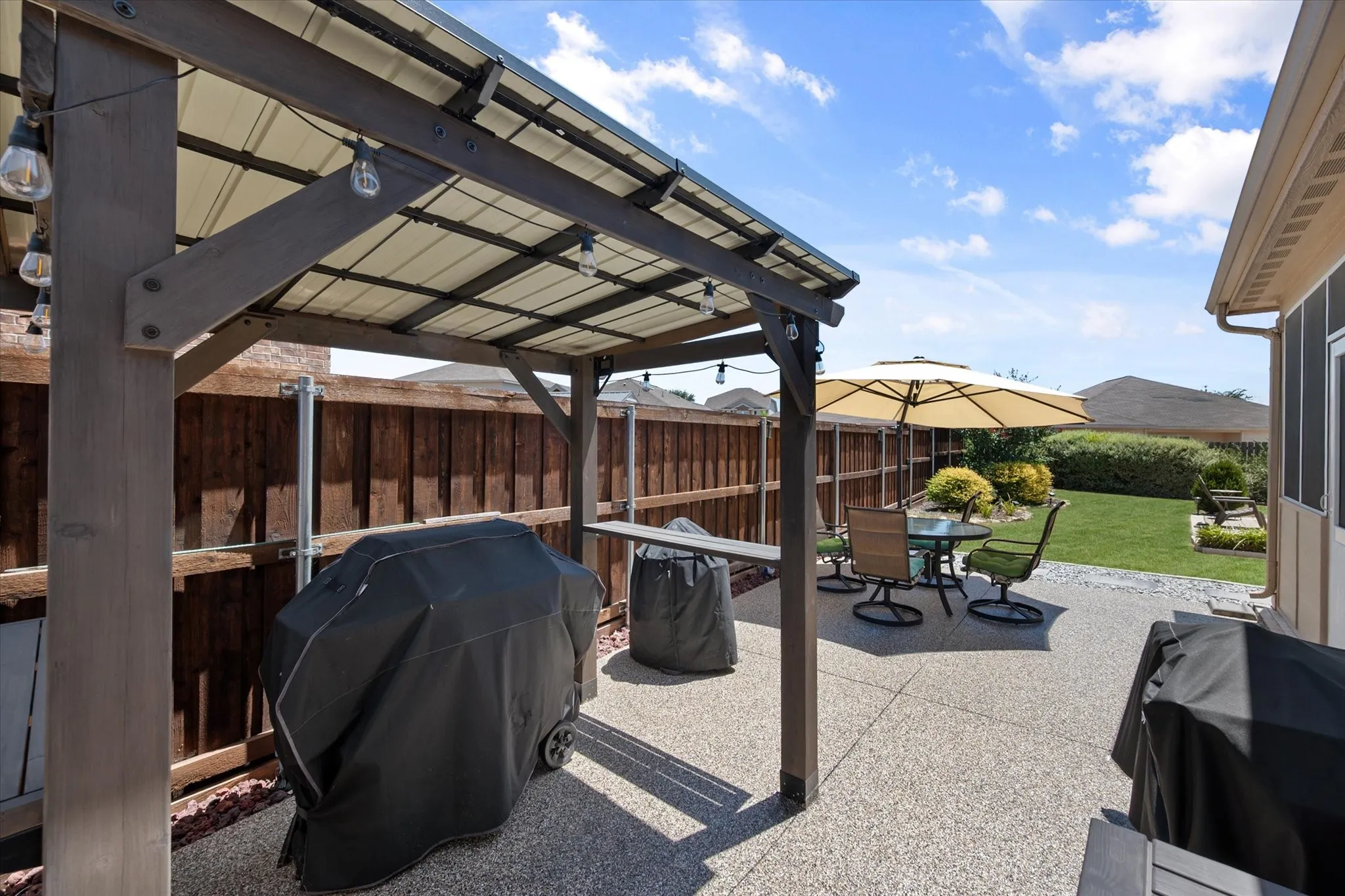 Expansive concrete patio featuring a wood-frame pergola with string lighting and a metal roof
