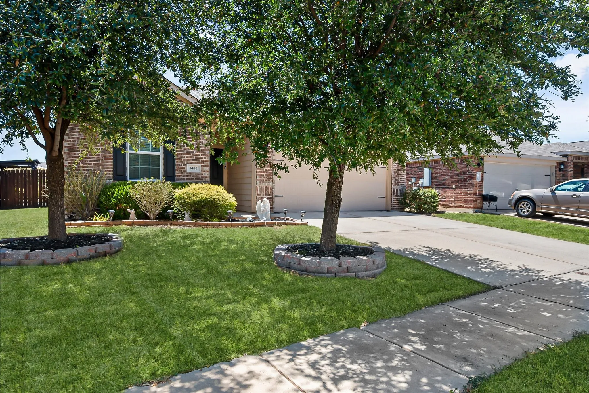 Brick exterior with a shuttered window, established trees, and a concrete driveway