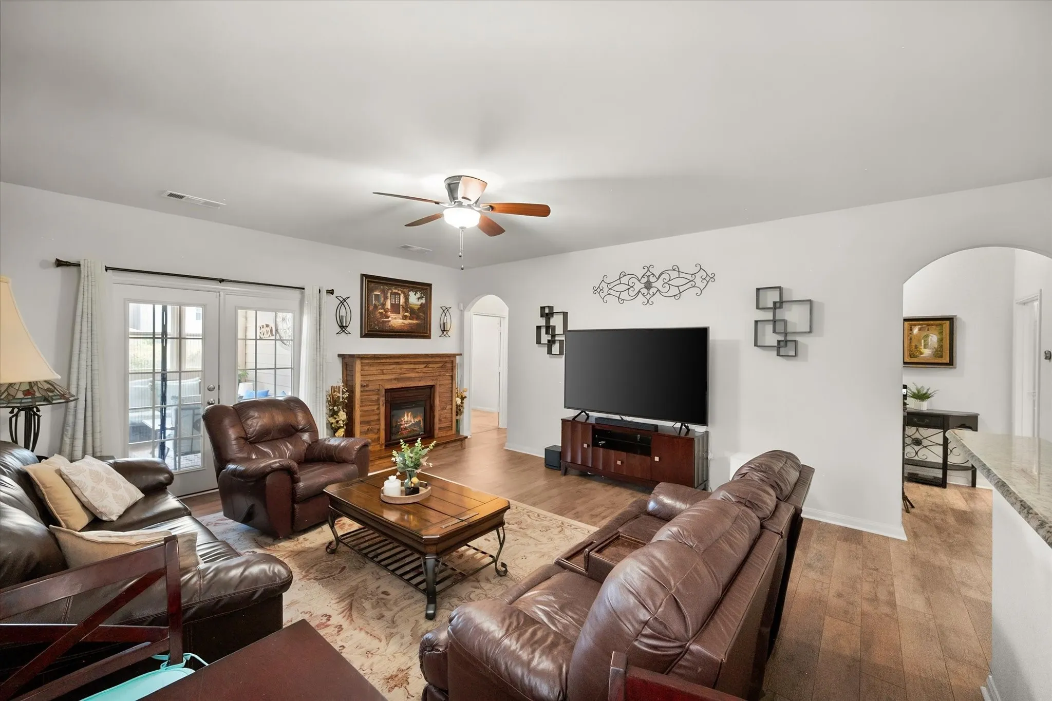 Wood-finish flooring throughout, a faux fireplace with a wood surround, white walls, and an arched doorway