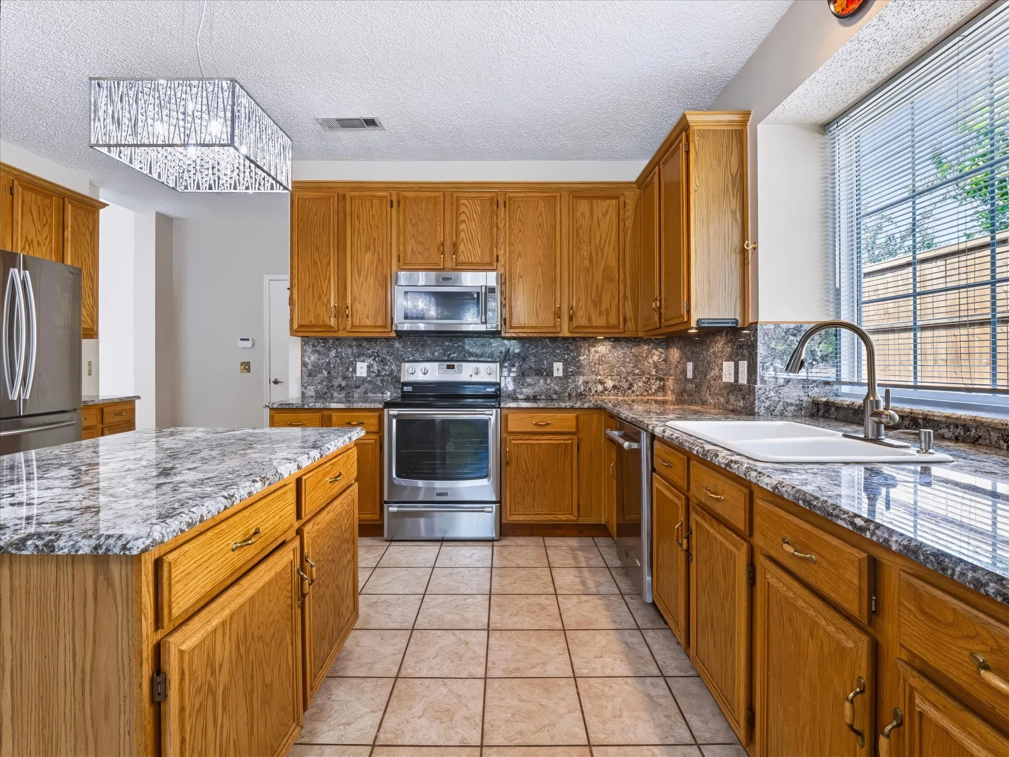 Kitchen featuring granite countertops, wood cabinetry, stainless steel appliances, a center island, and tile flooring