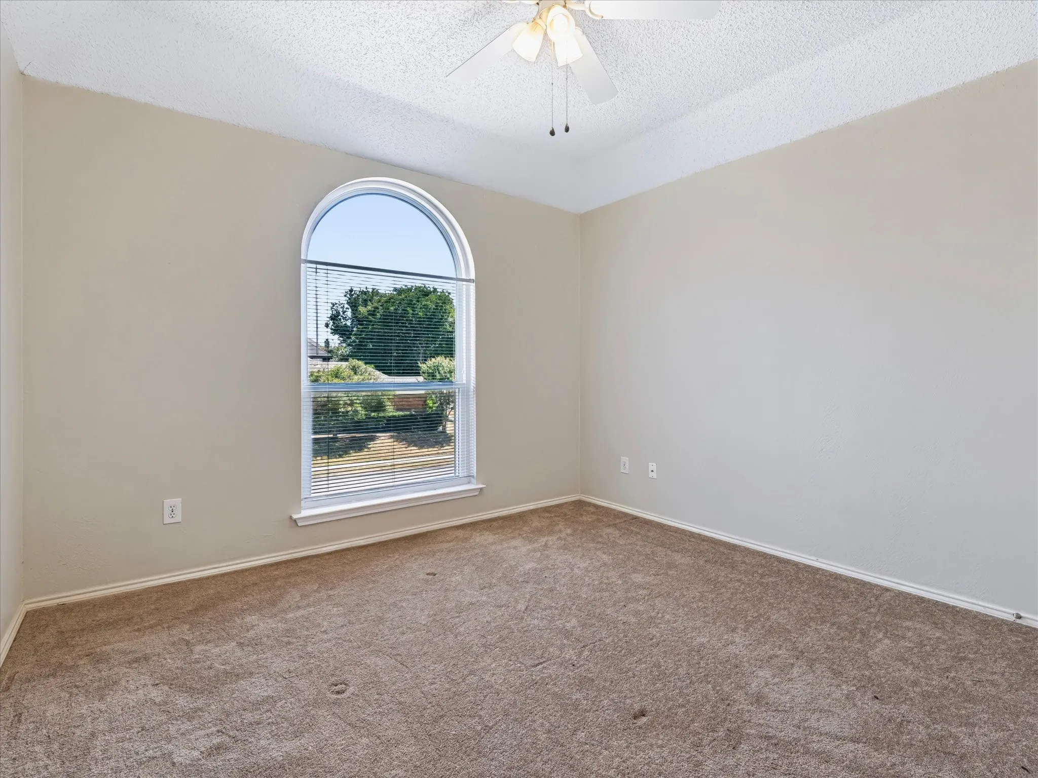 Arched window with blinds, carpeted flooring, neutral wall paint, and a ceiling fan with integrated lighting