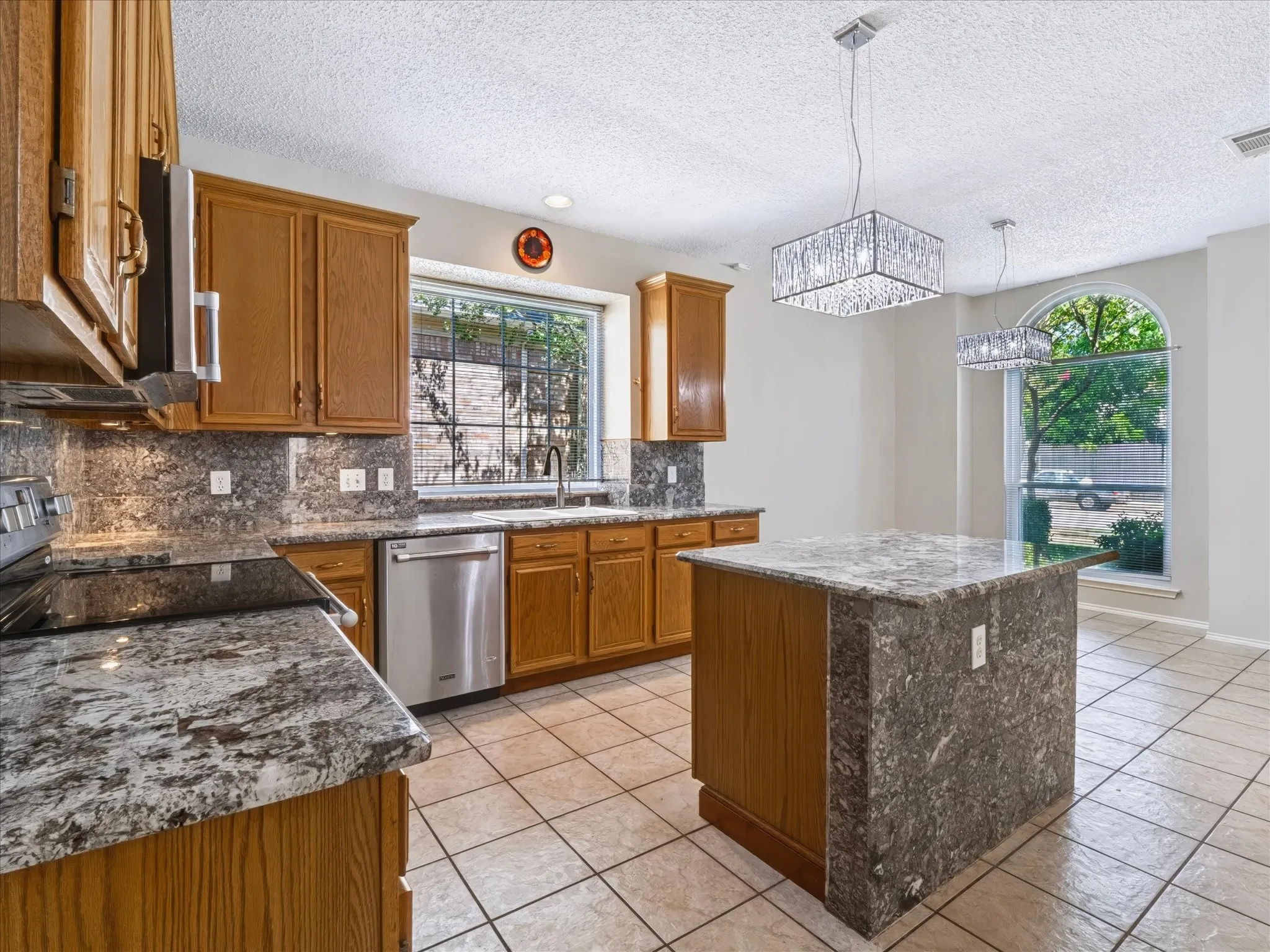 Kitchen featuring wood cabinetry, stainless steel dishwasher, tile flooring, and stone countertops