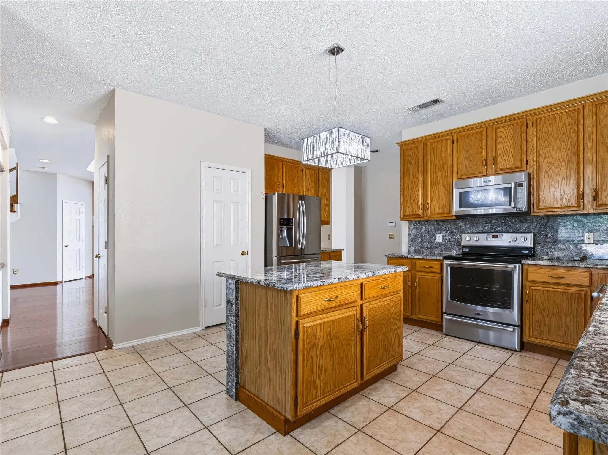 Kitchen featuring a central island with a granite countertop, wood cabinetry, stainless steel appliances, and tile flooring