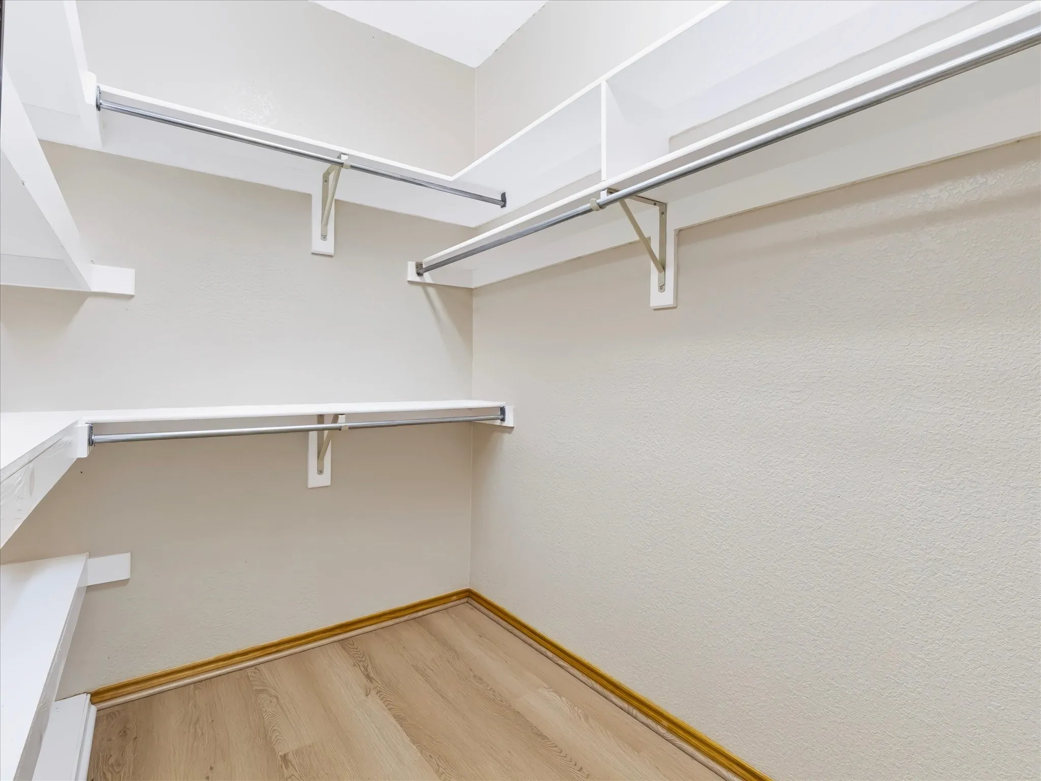 Spacious walk-in closet featuring multiple chrome-finished hanging rods at varying heights, wooden-finish flooring, and soft-close bracket hardware for organized storage and accessibility