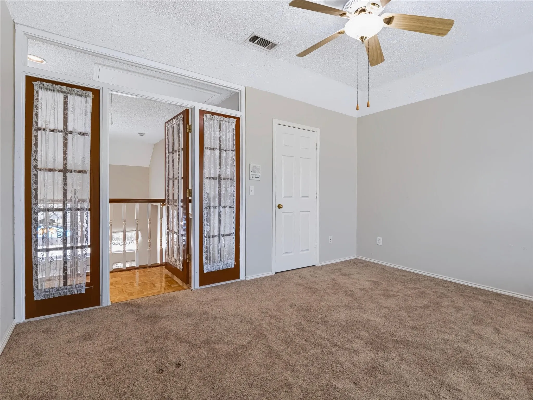 Brown carpet flooring, neutral painted walls, ceiling fan, white paneled door, and glass panel French doors