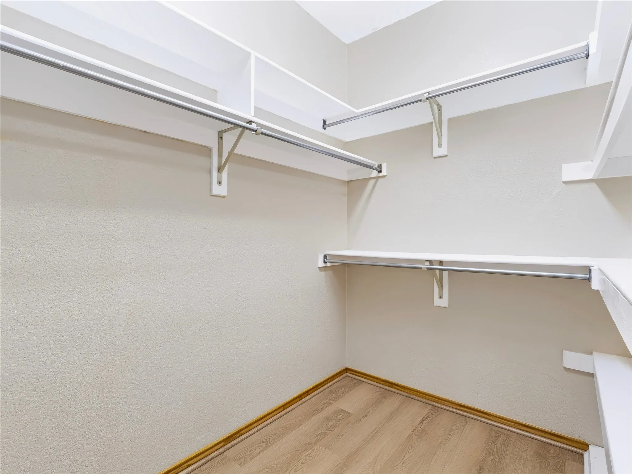 Walk-in closet with multiple white shelving units, integrated hanging rods, and wood-finish flooring