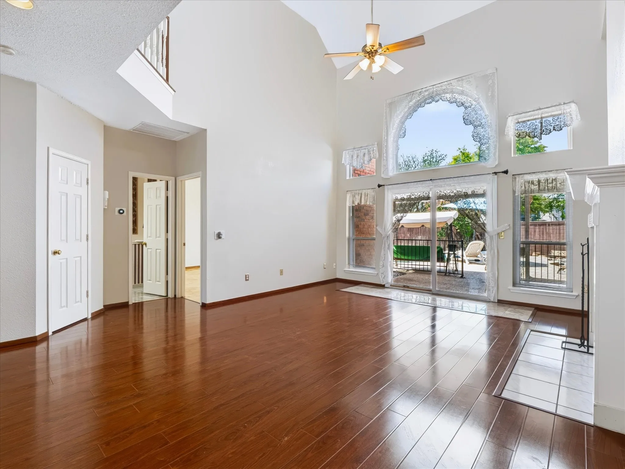 Soaring vaulted ceiling, wood-finish flooring, multiple large windows, sliding glass patio doors, and a fireplace with a tile hearth