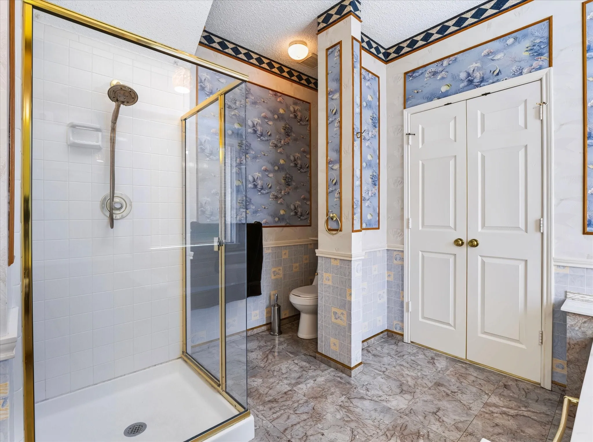 Glass-enclosed shower with gold-tone hardware, white shower pan, and white subway tile surround