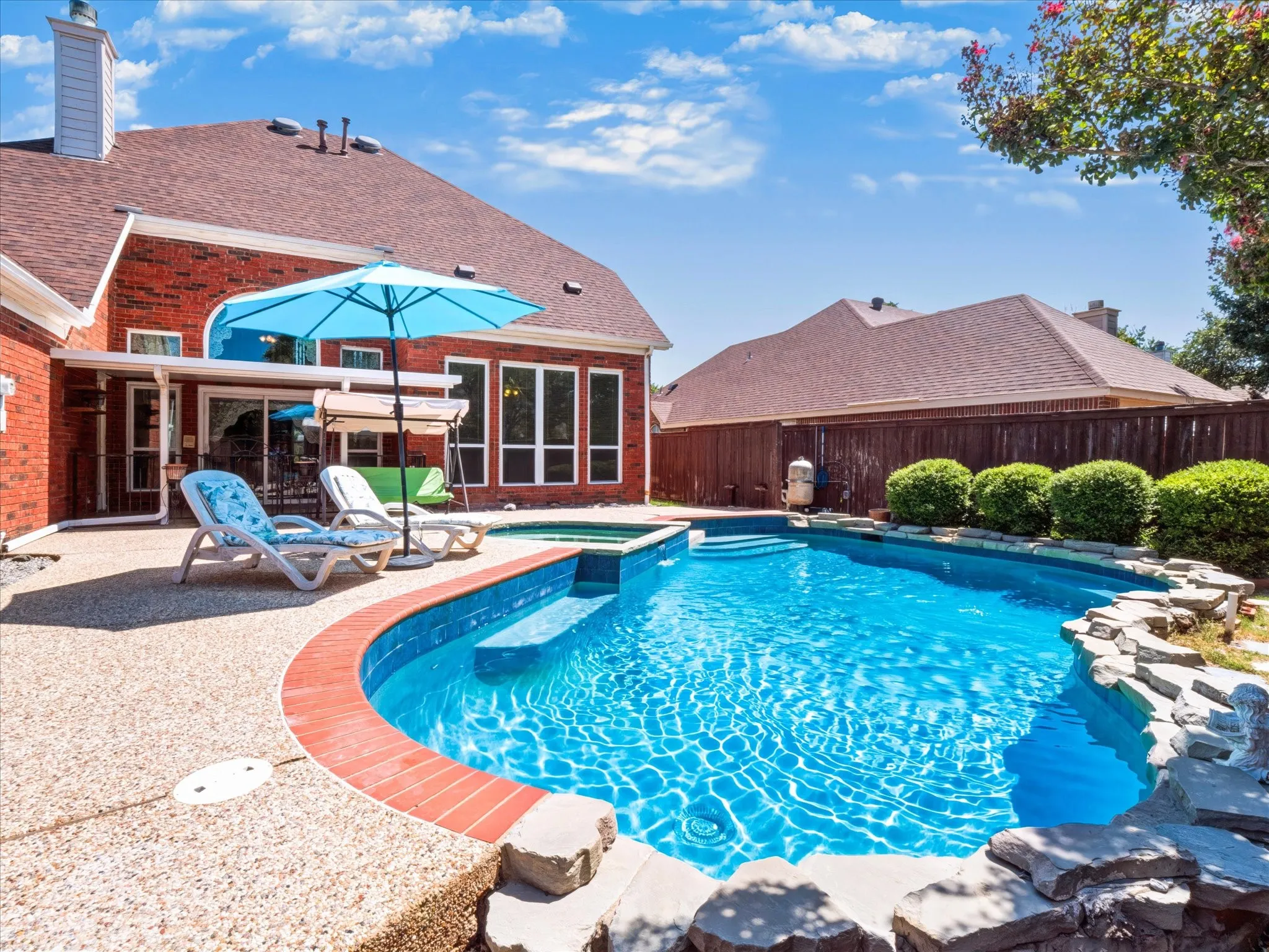 Private backyard with a built-in swimming pool, integrated spa, and surrounding rock landscaping