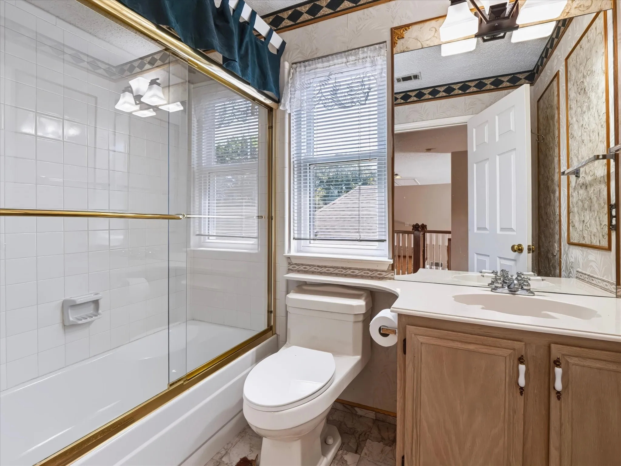 White tile bathtub with gold-toned sliding glass shower door