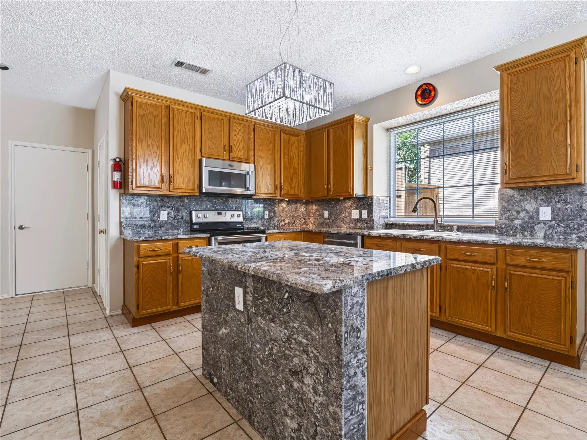 Kitchen featuring a large window, tile flooring, wood cabinetry, a central island with a stone countertop, and an undermount sink