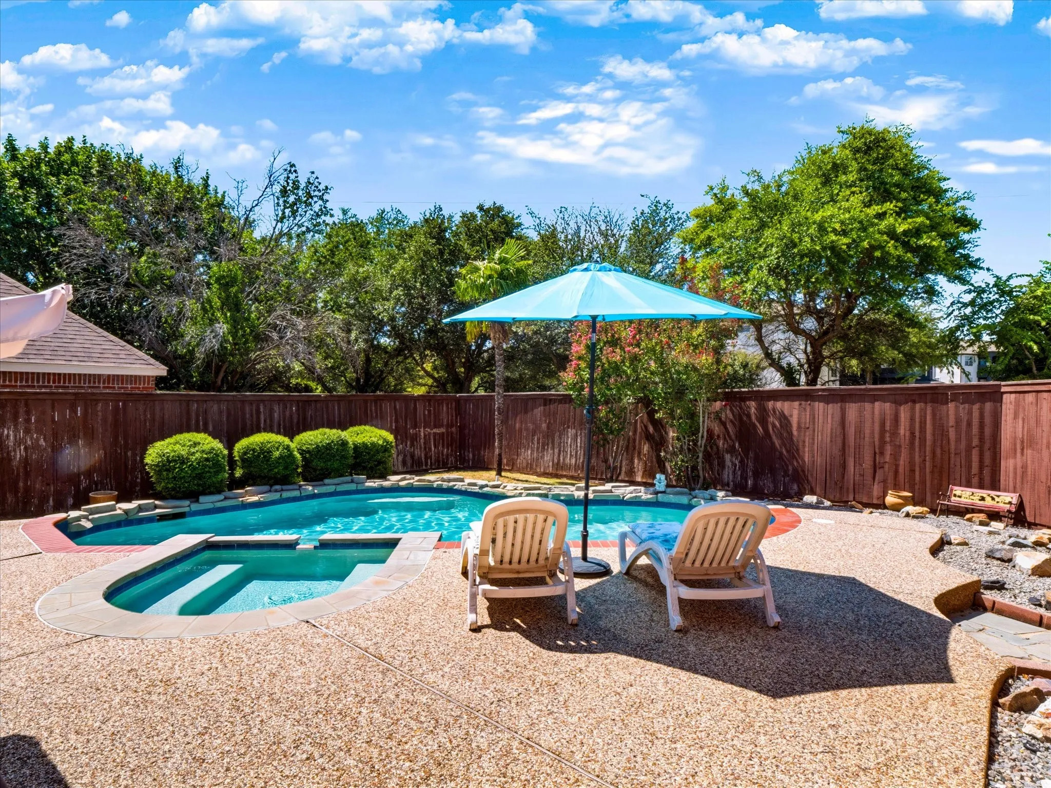 Swimming pool with built-in spa, exposed aggregate patio, wood fencing, and mature landscaping