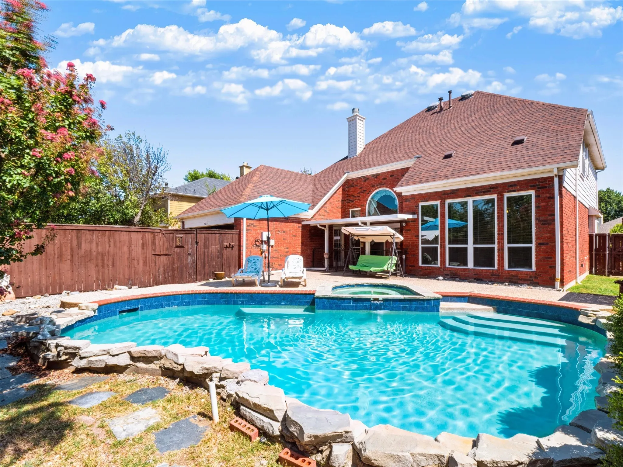 Brick exterior featuring a private fenced yard, a large swimming pool with integrated spa, and multiple floor-to-ceiling windows