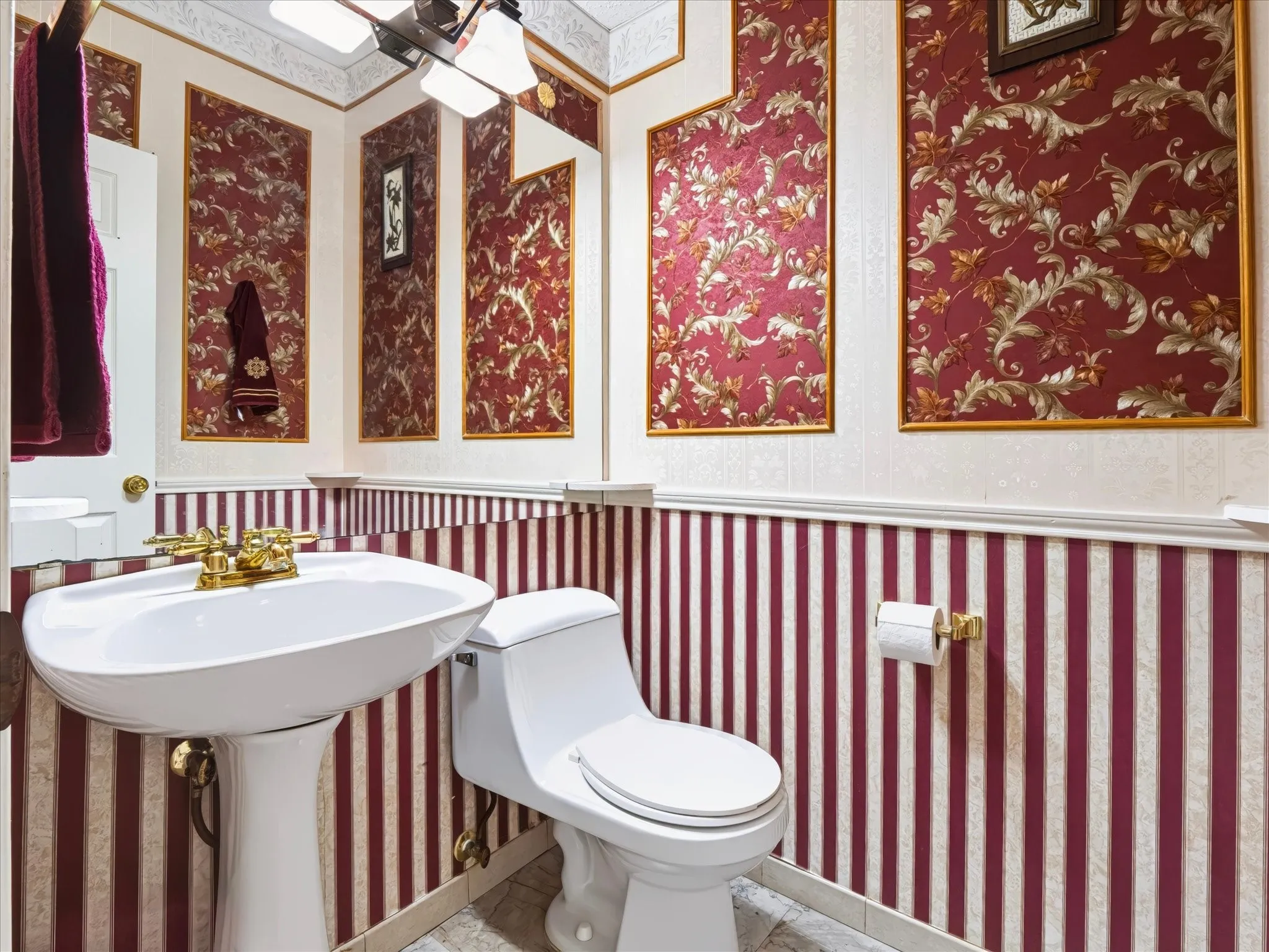 White pedestal sink with brass-finish faucet, toilet with white toilet seat, and decorative wall coverings