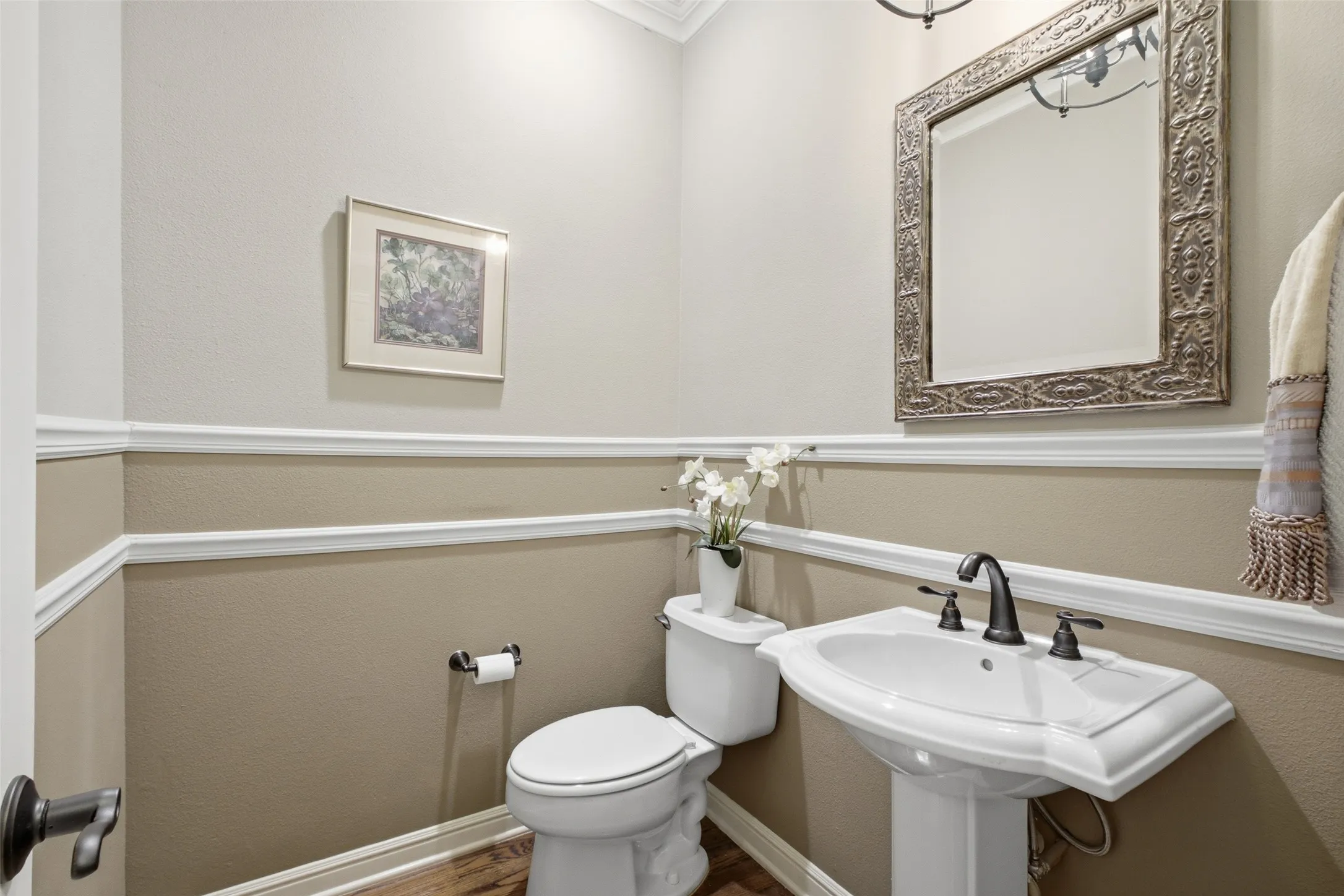 Pedestal sink with dark bronze fixtures, white commode, detailed wall trim, and wood-finish flooring