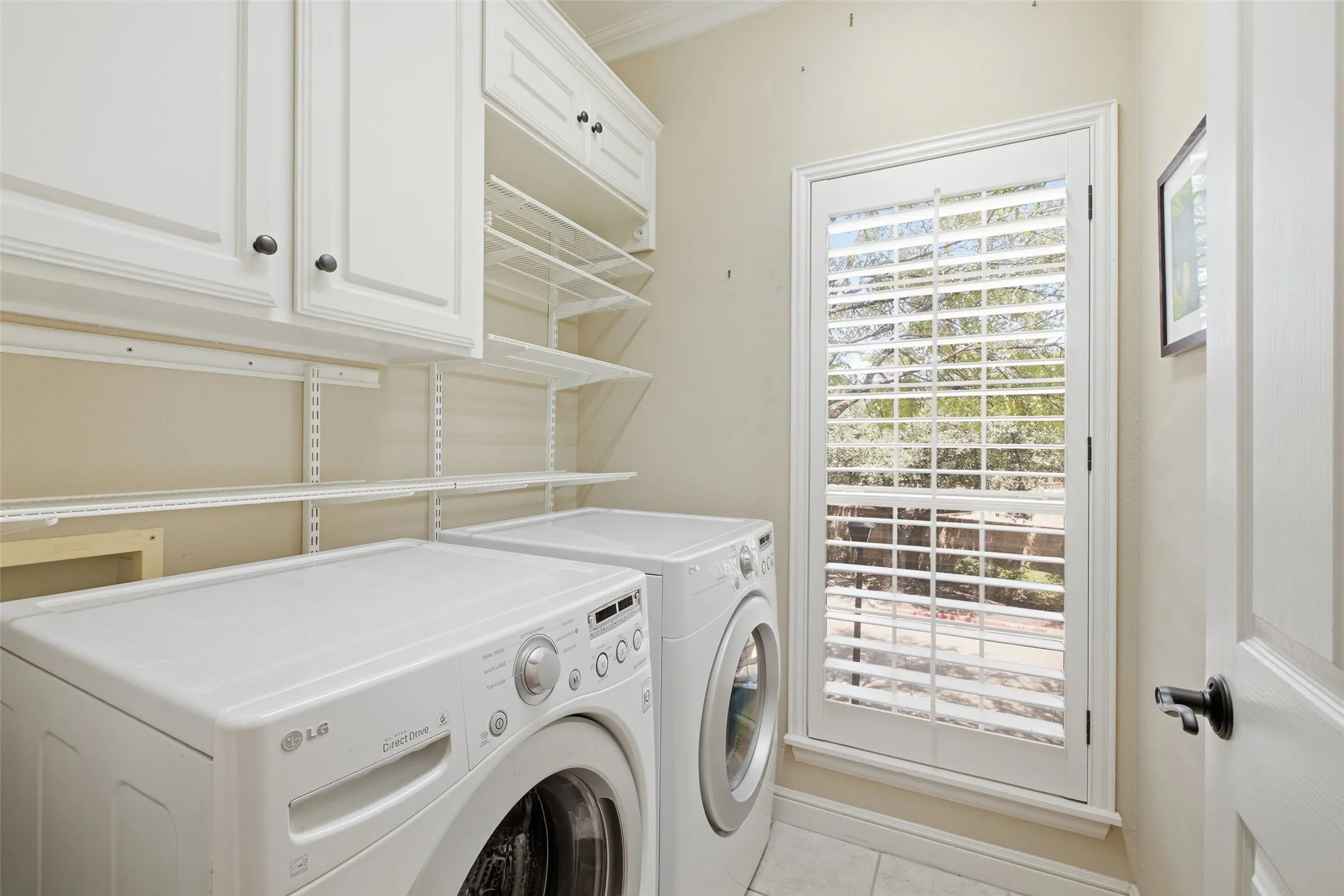 White cabinetry with dark hardware, adjustable shelving, and a glass-paneled door with plantation shutters