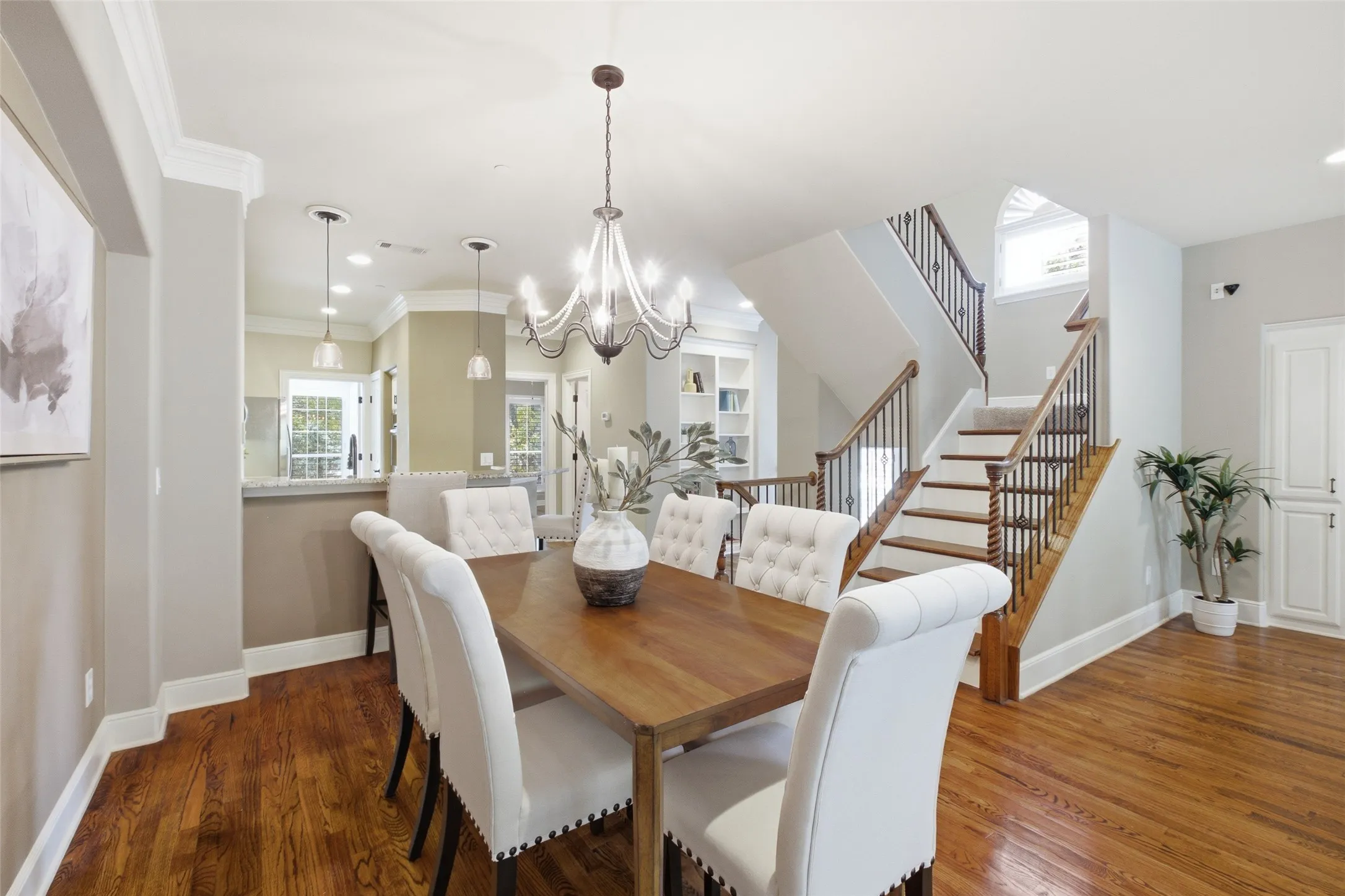 Hardwood flooring, elegant chandelier, built-in shelving, two-tone staircase, and crown molding