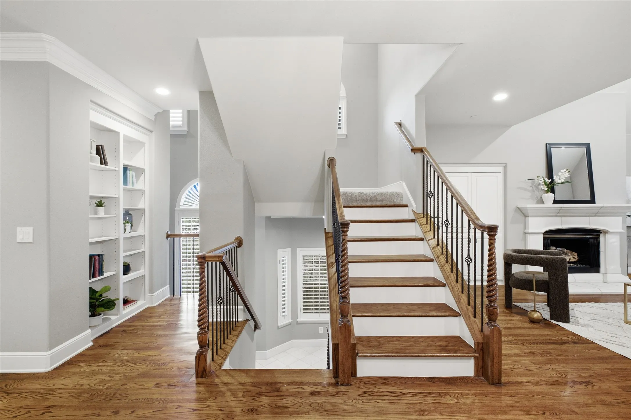 Hardwood flooring, custom built-in shelving, wrought iron balusters, white mantel, and arched window