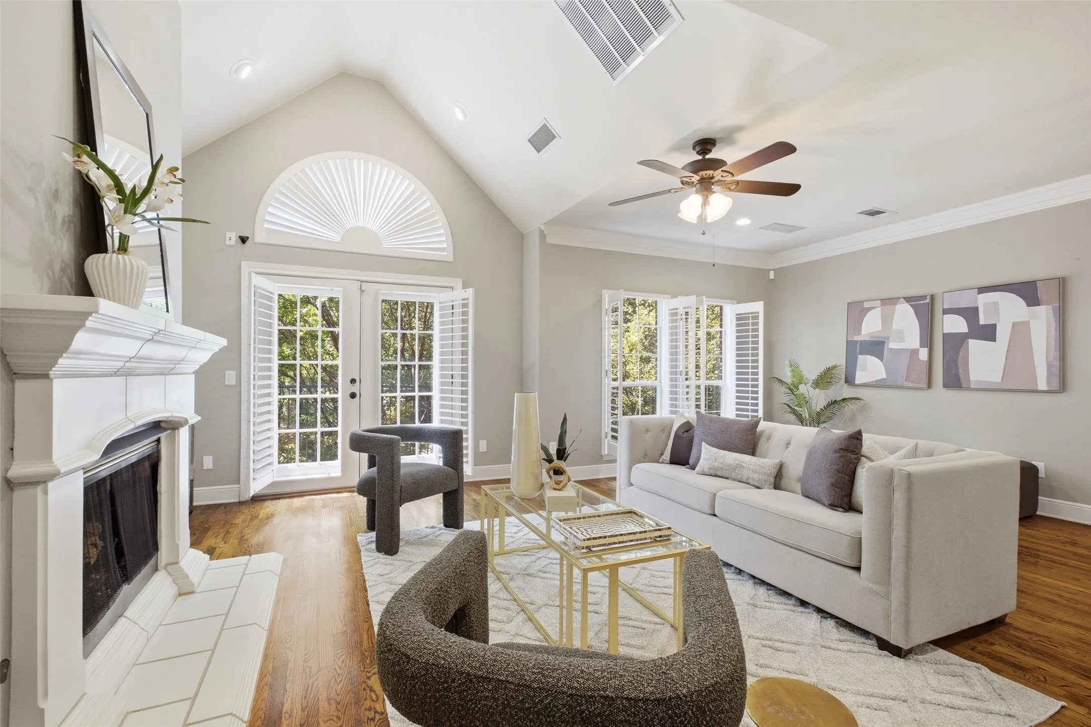 Vaulted ceiling featuring a skylight, wood-finish flooring, white fireplace with tile surround, and double French doors with transom window and interior shutters