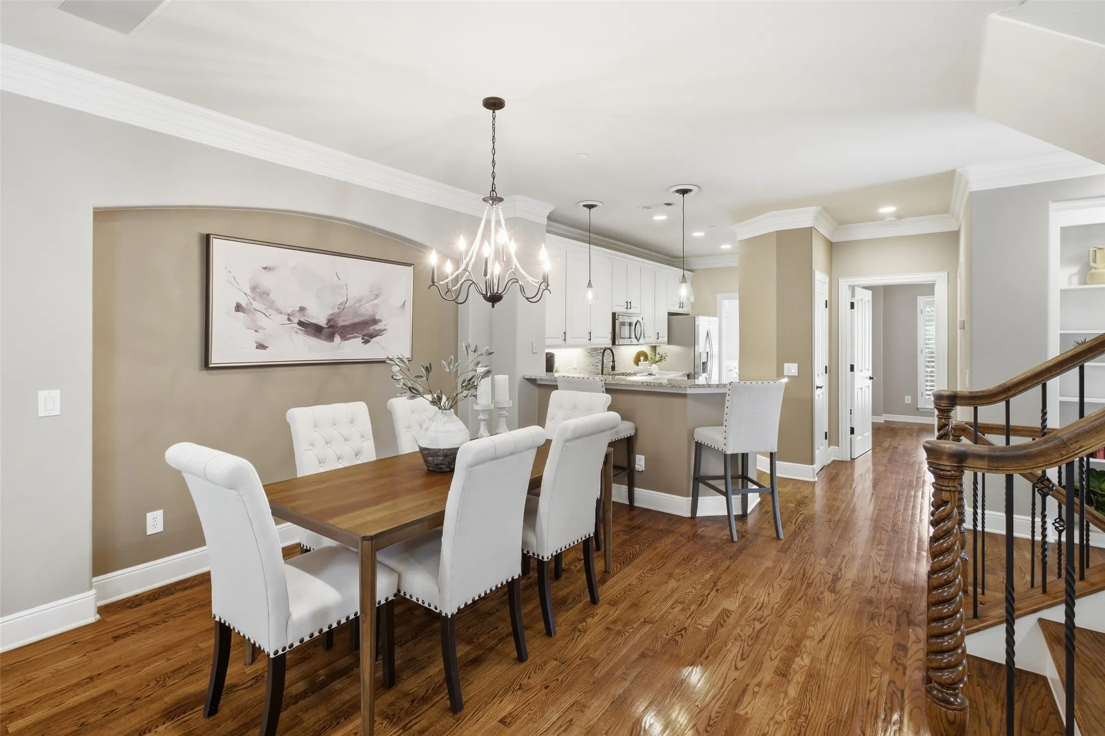 Hardwood flooring throughout, crown molding, built-in shelving, white cabinetry, and a kitchen island with bar seating