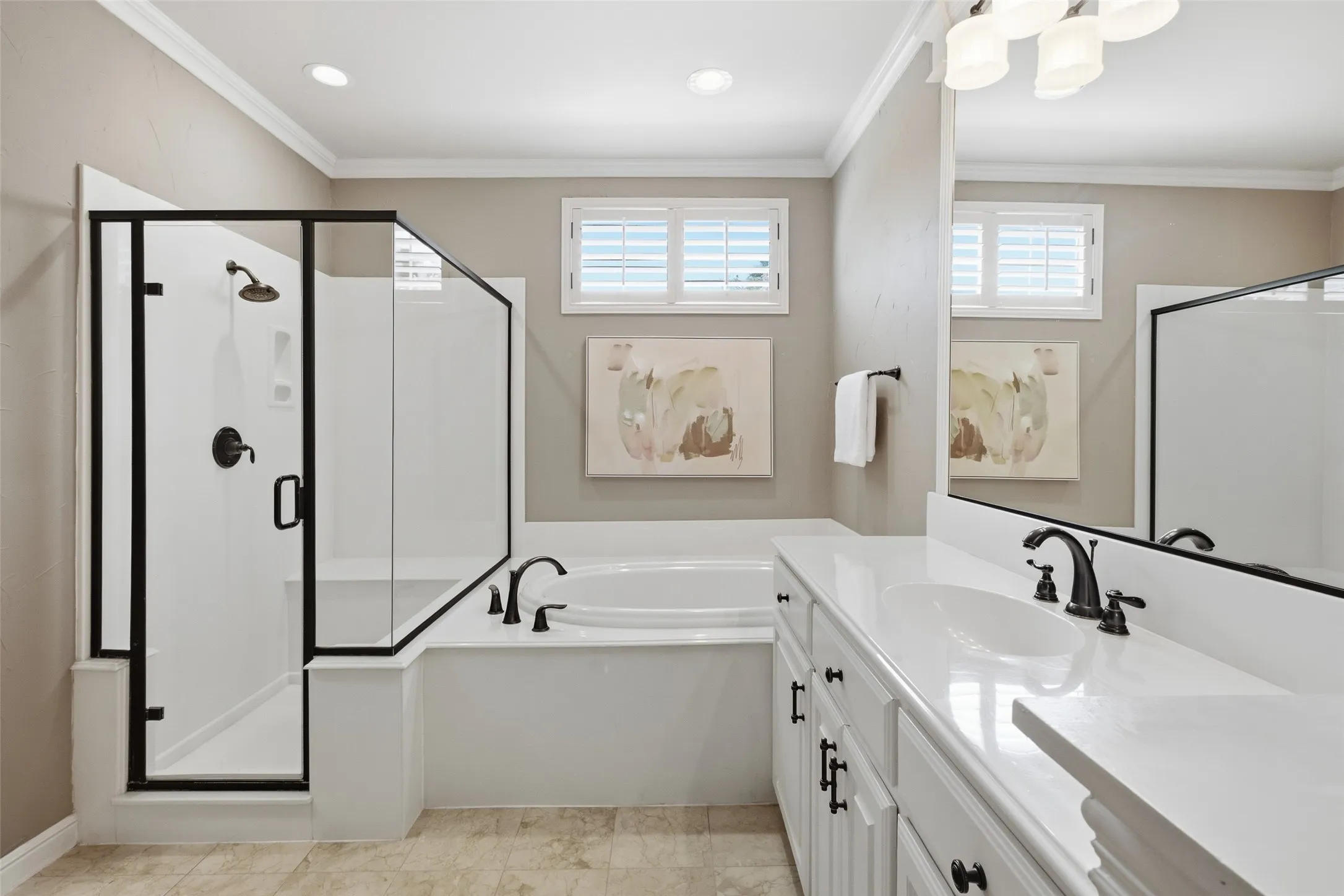 Shower enclosure with black framing, built-in soaking tub, dual windows with plantation shutters, vanity with white countertop, and dark-finish fixtures