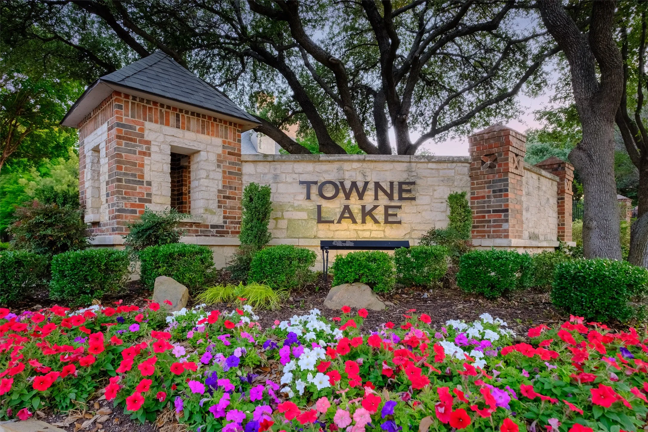 Stone and brick entryway with a peaked roof structure, integrated signage, and mature trees