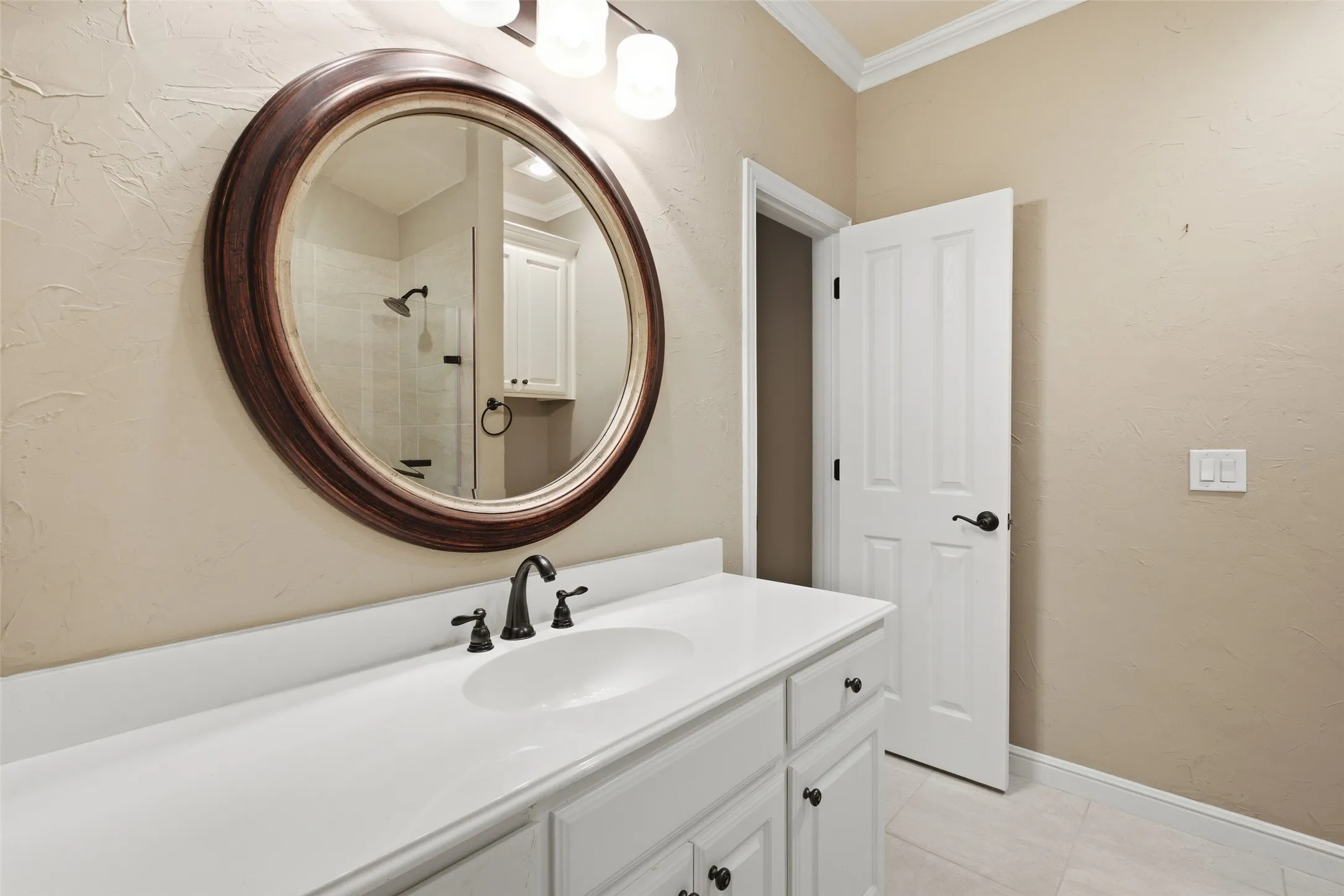 White vanity with integrated sink, oil-rubbed bronze faucet, and a large round mirror with a wood frame