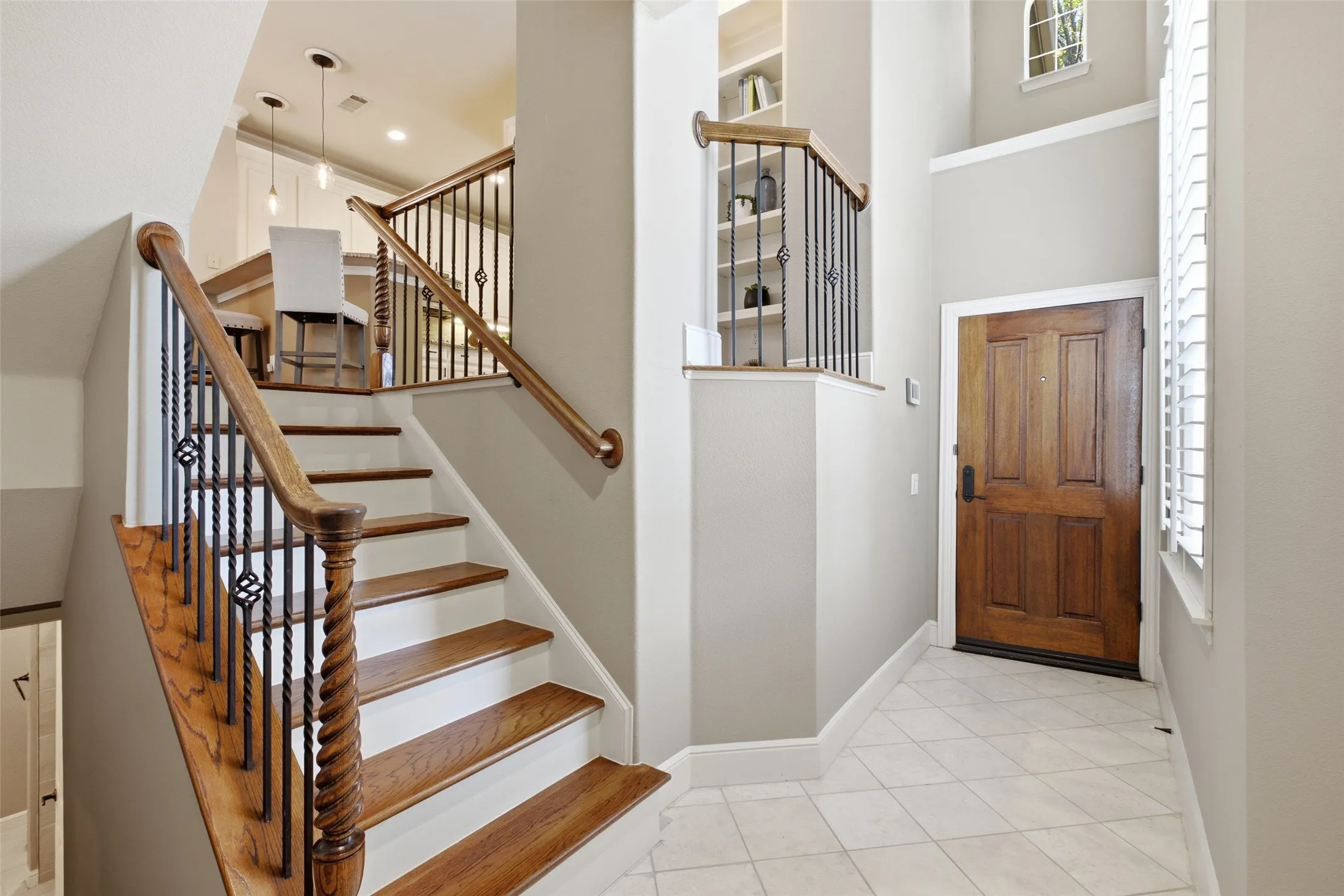 Hardwood staircase with wrought iron balusters, natural wood entry door, tile flooring, and built-in shelving