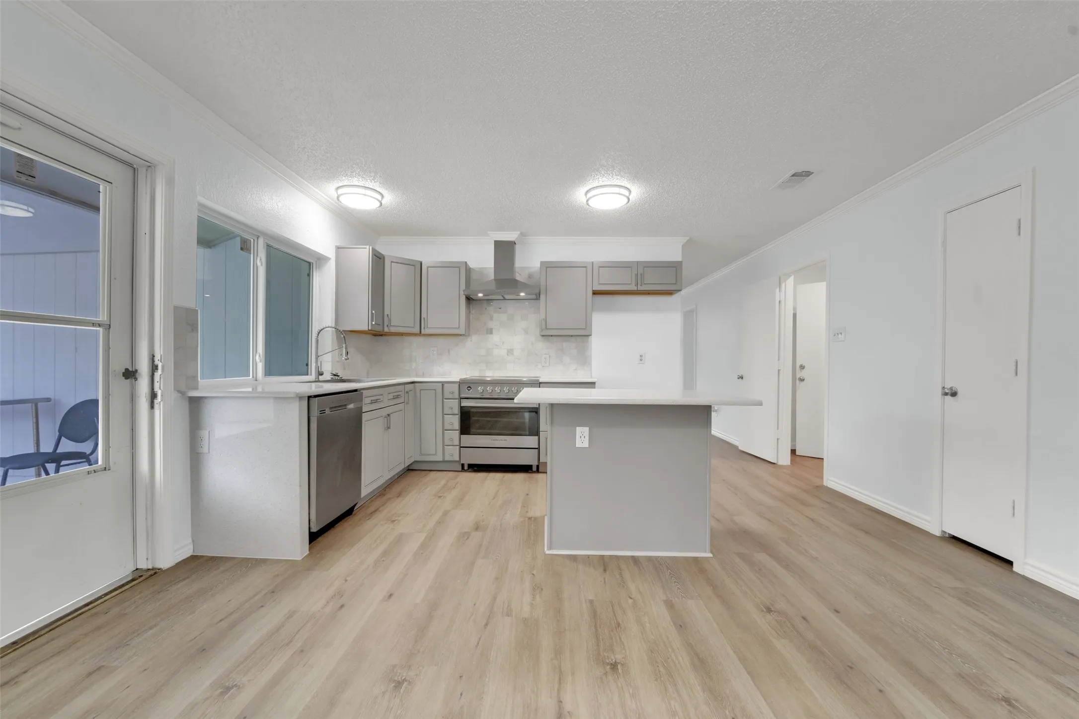 Modern kitchen featuring gray cabinetry, stainless steel appliances, light wood-finish flooring, and a central island with countertop seating